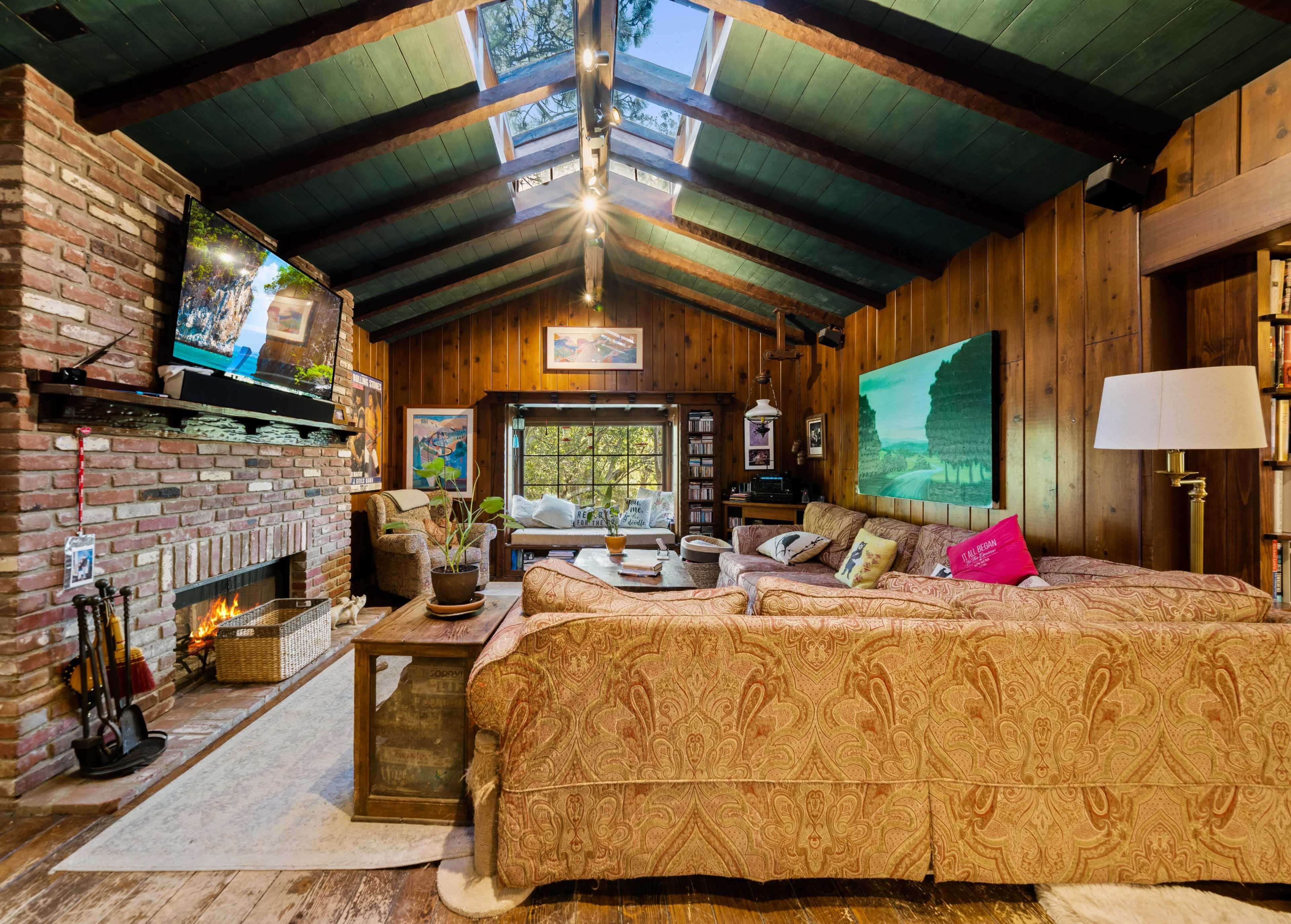 The living room features a brick fireplace, a large sectional sofa, wooden walls, and a skylighted ceiling.