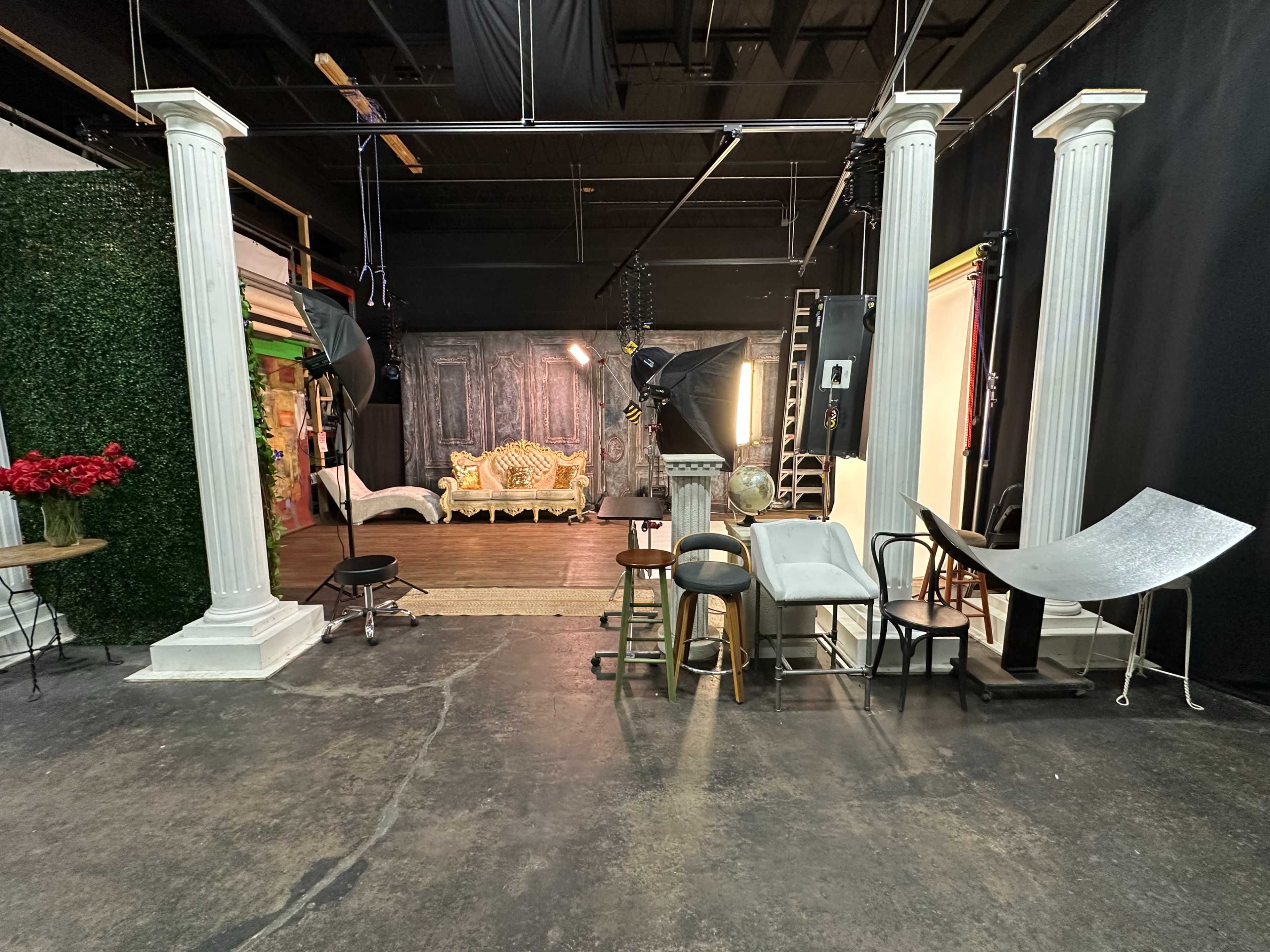 The image shows a photography studio with decorative columns, various chairs, and backdrop setups.