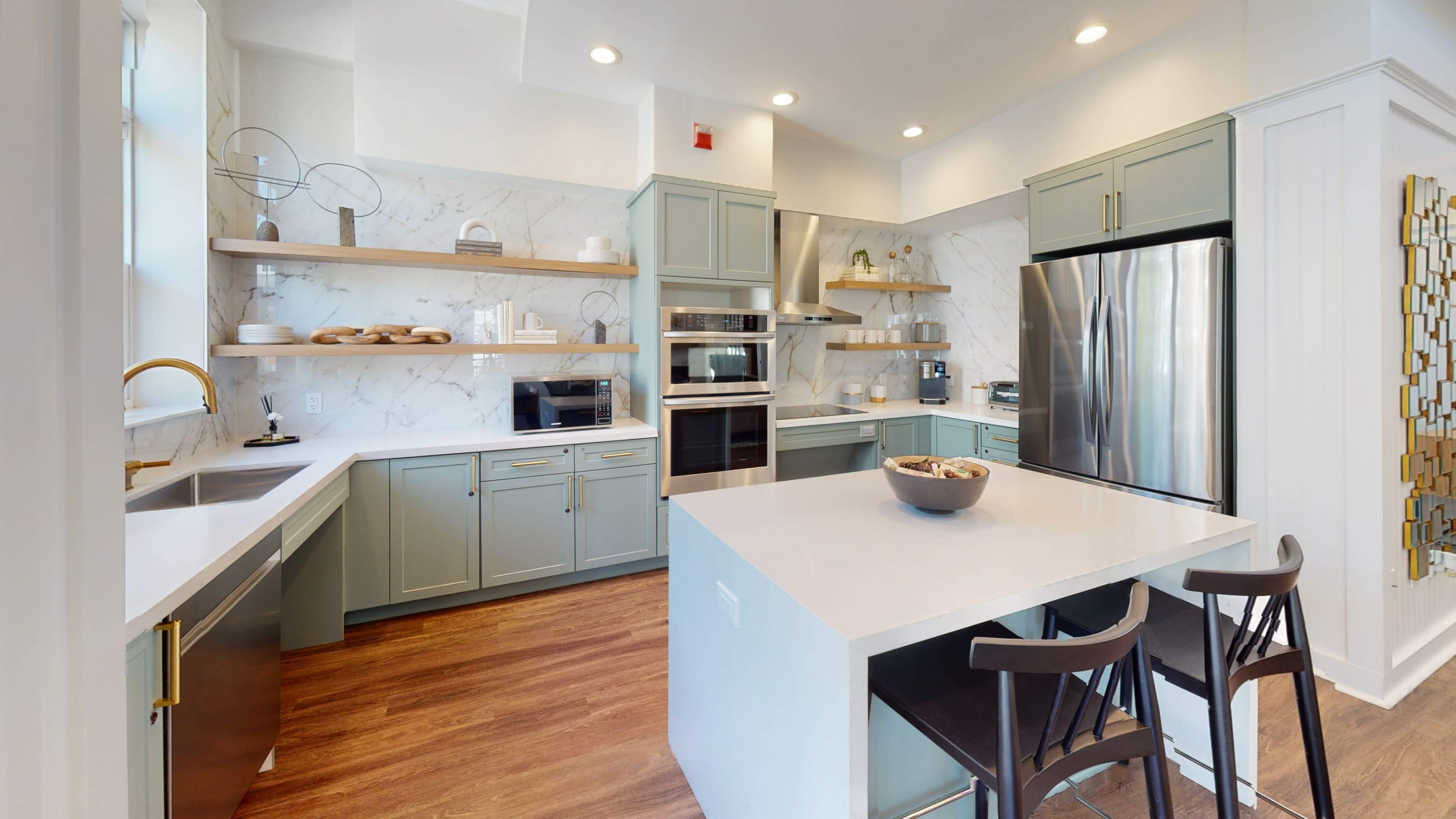 A modern kitchen featuring light green cabinetry, stainless steel appliances, and a large island with bar stools.