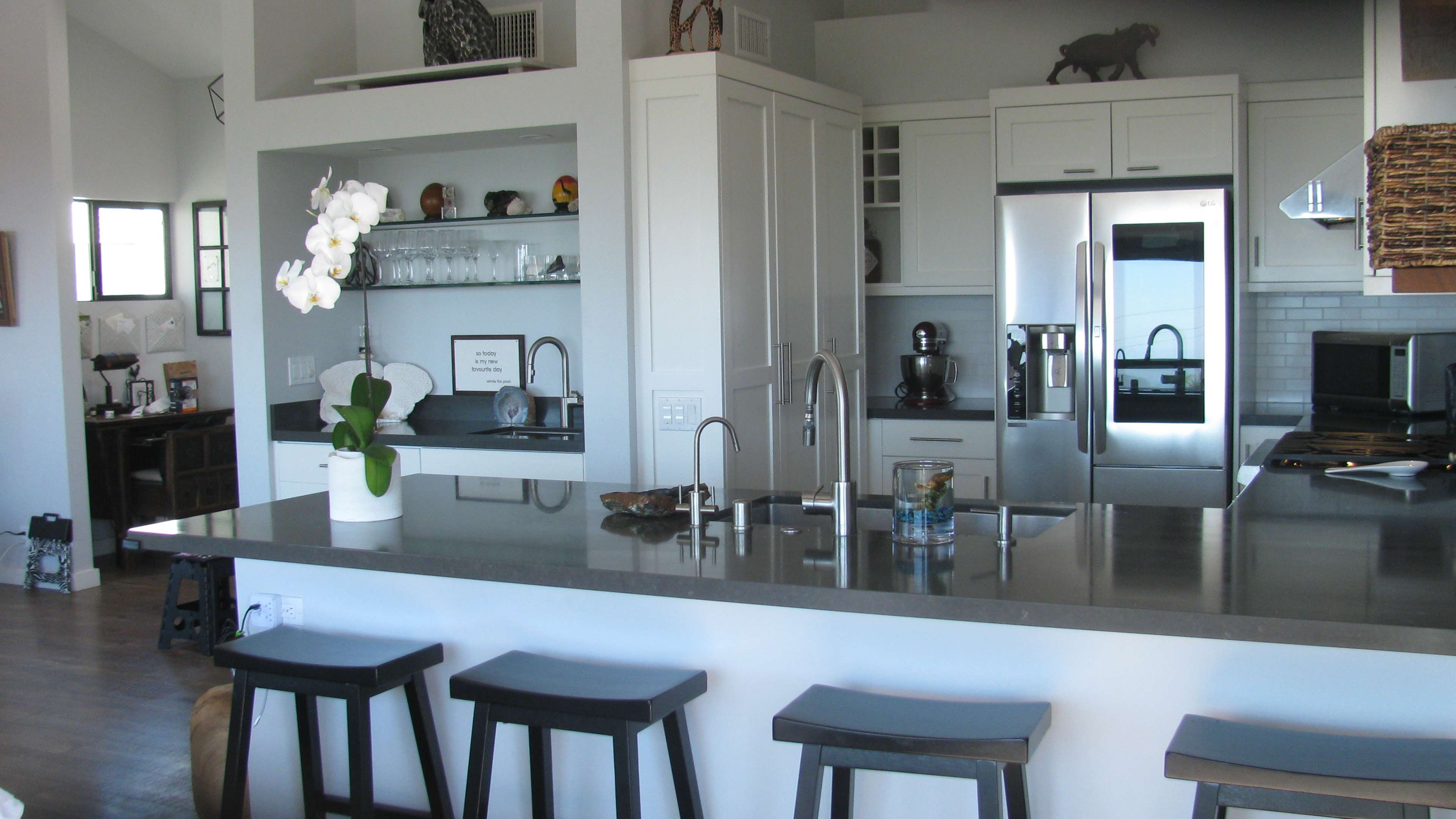A modern kitchen with a large island, sleek appliances, and a small dining area visible in the background.