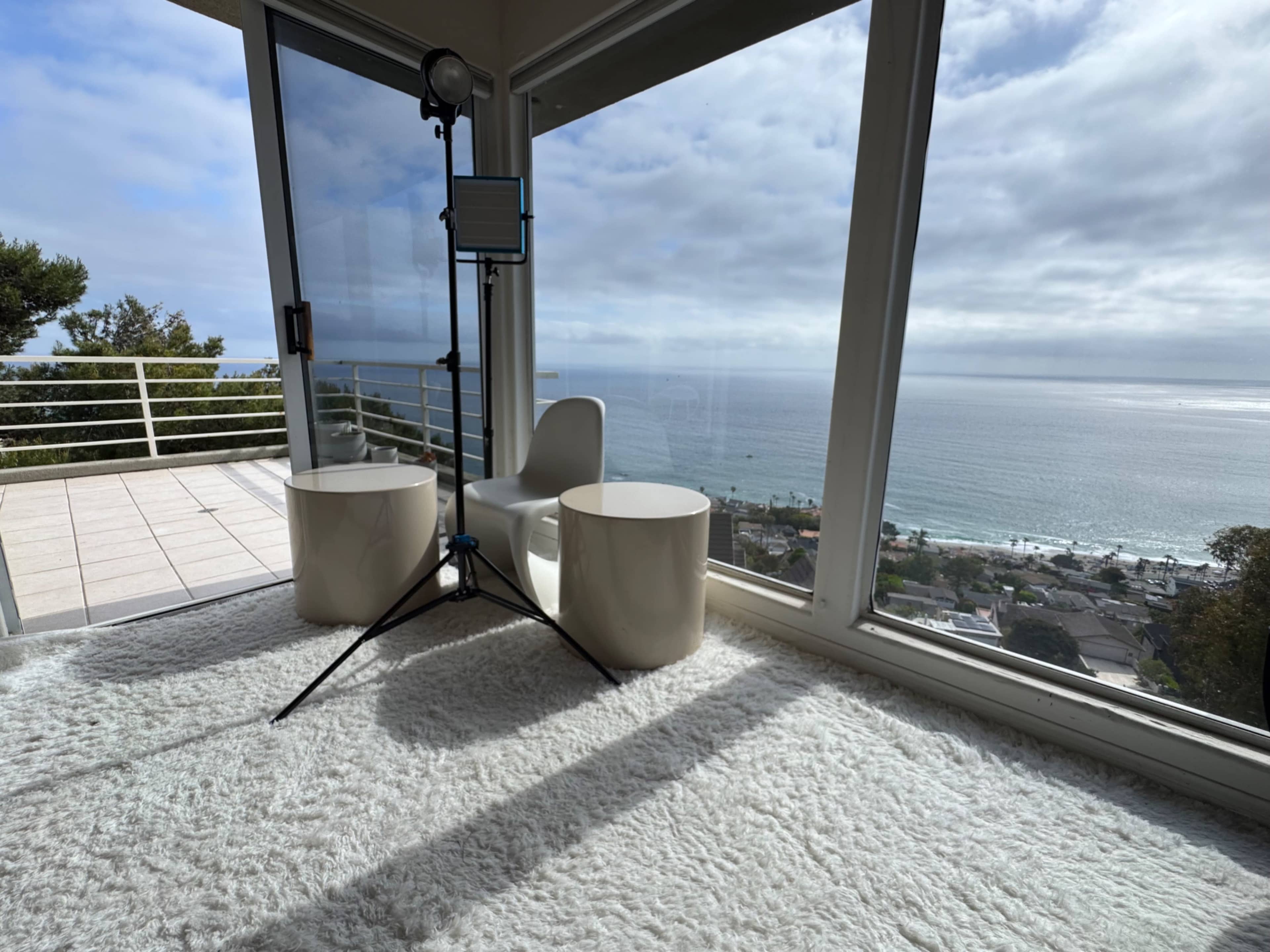 A stylish interior with two white modern chairs and a lighting stand overlooks a view of the ocean through large windows.