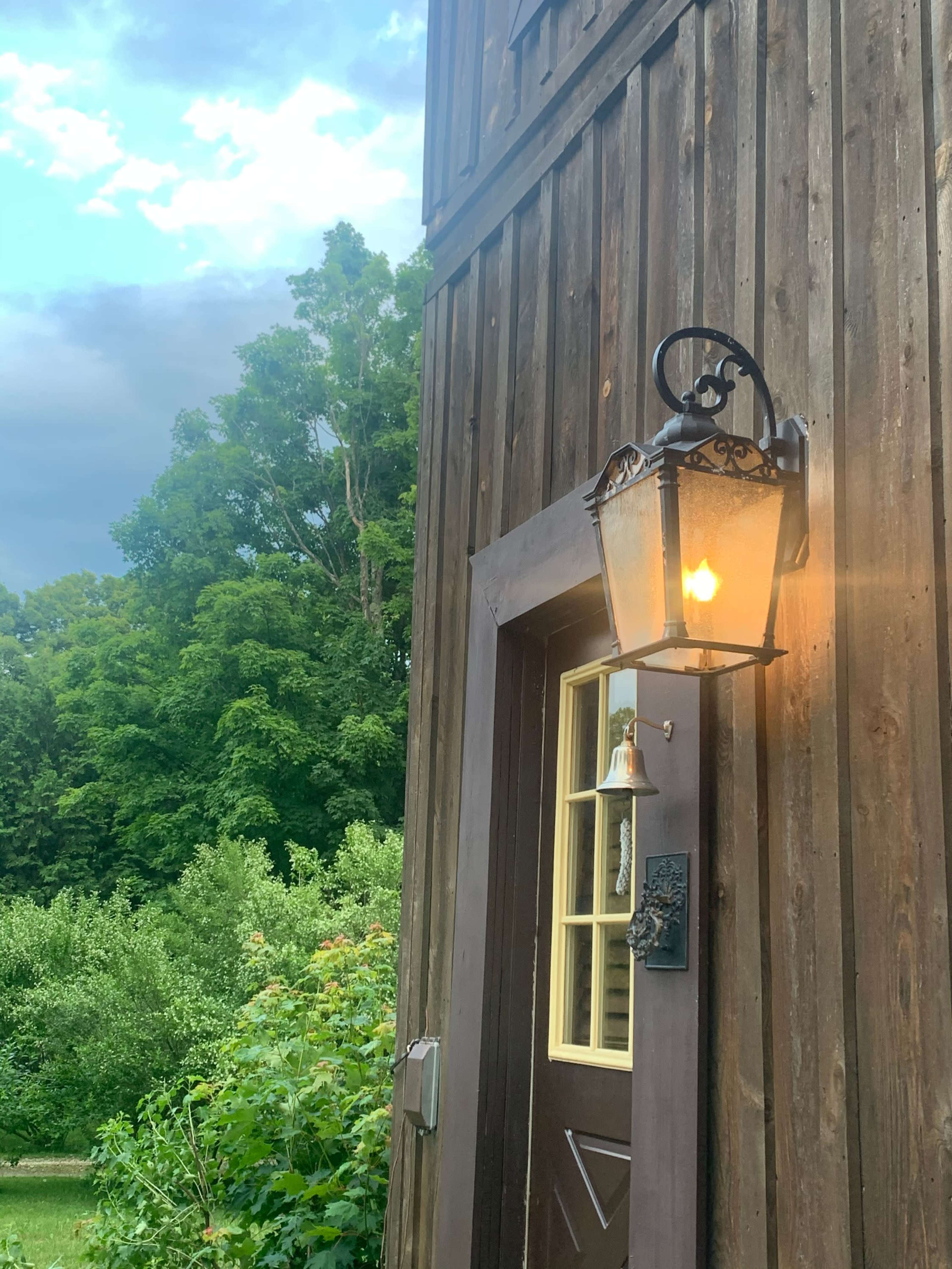A wall-mounted lantern illuminates a wooden door on a rustic building surrounded by greenery.