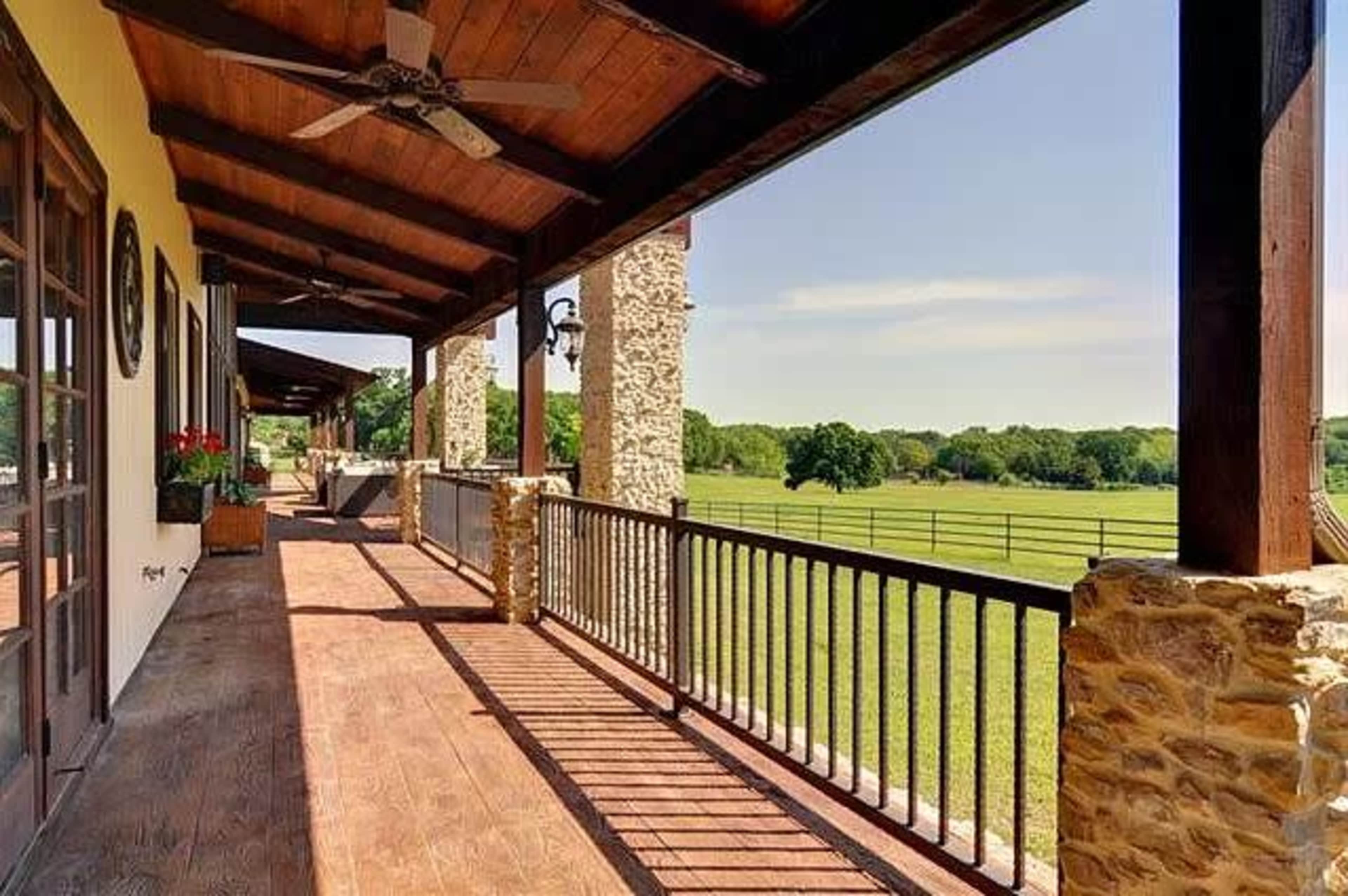 A covered porch with wooden beams, stone pillars, and a view of a grassy field and trees in the background.
