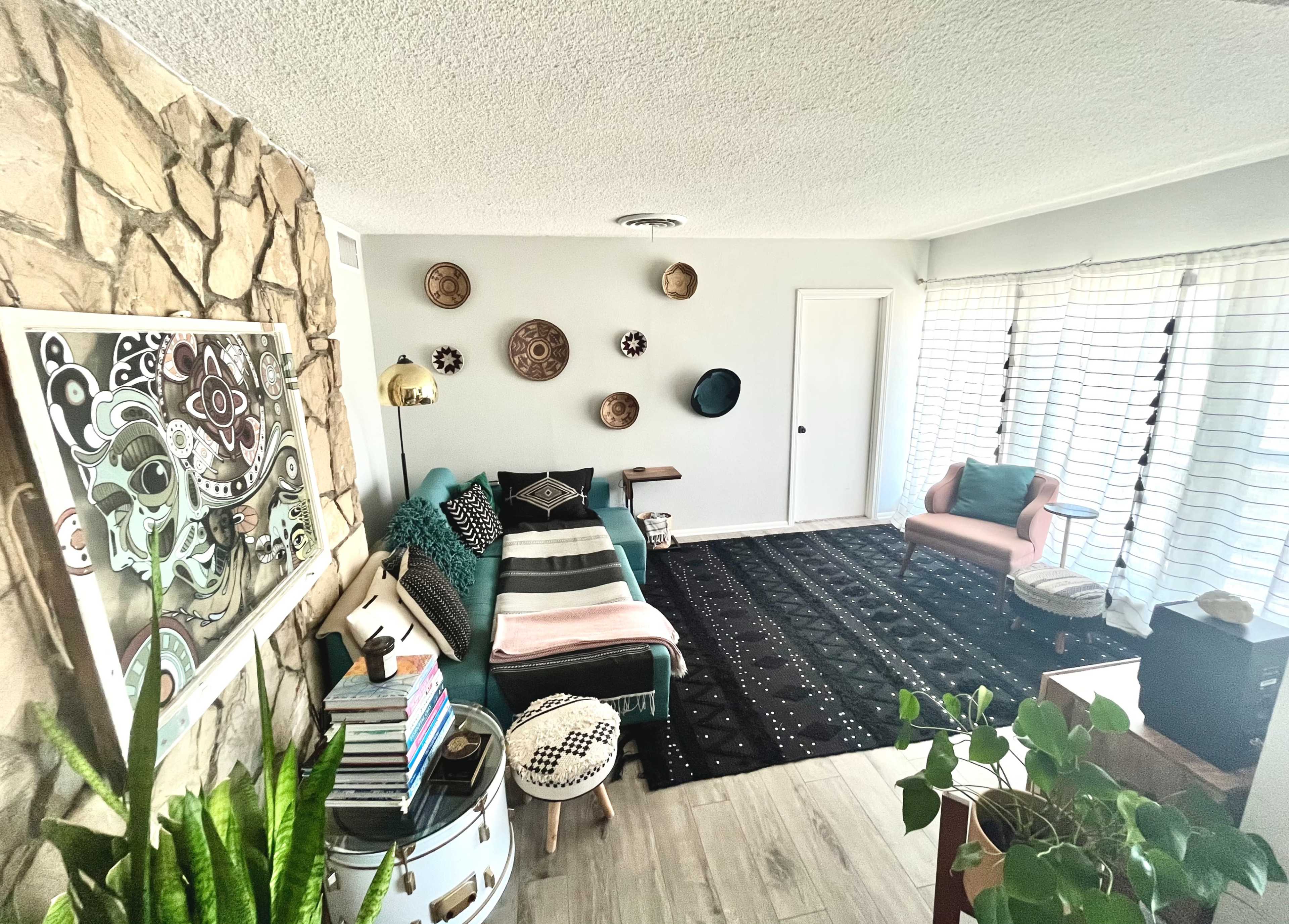A modern living room featuring a stone accent wall, a teal sofa, an area rug, and various decorative wall plates.