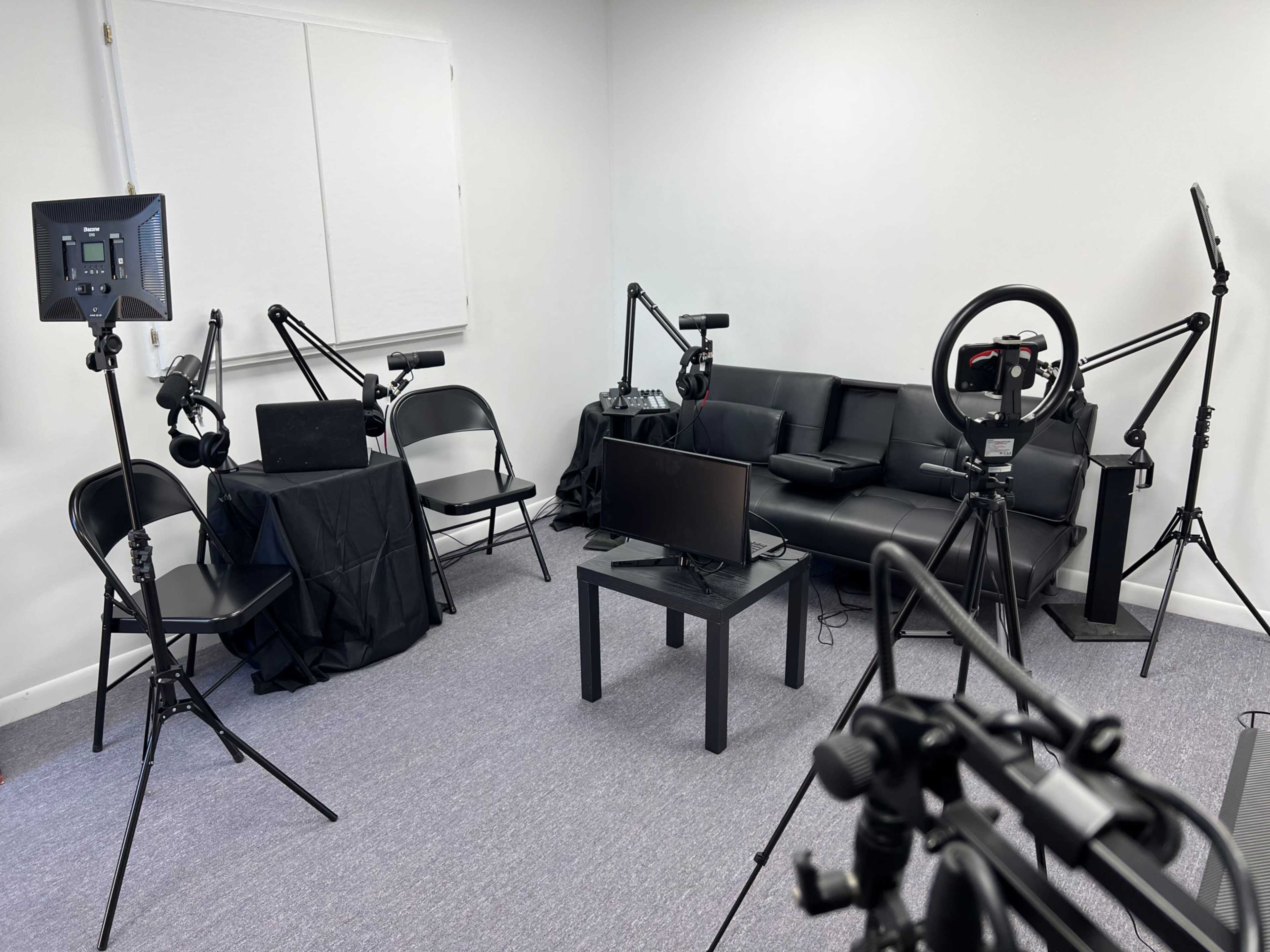 A recording studio setup with a black couch, a table, a television, and several audio and video equipment stands arranged around the room.