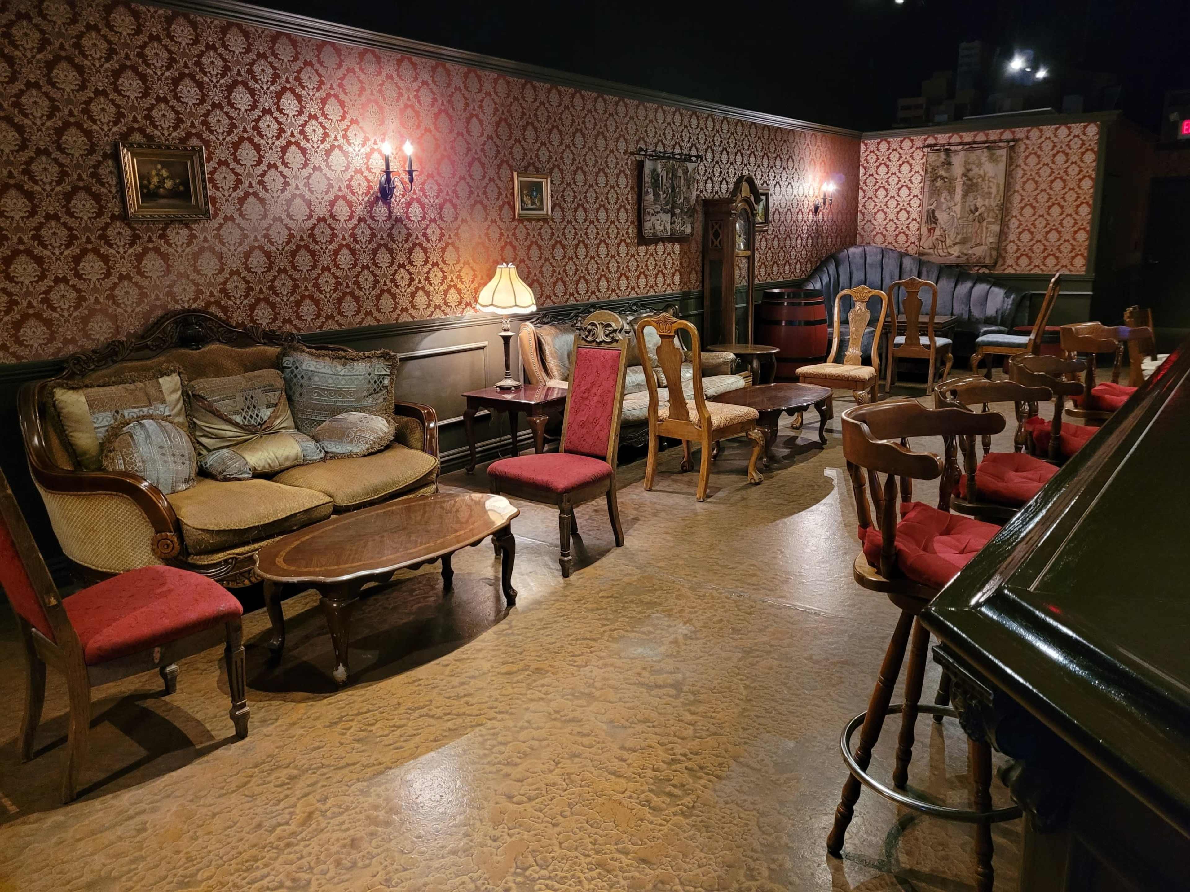A vintage-style seating arrangement in a dimly lit room with patterned wallpaper and various chairs and tables.