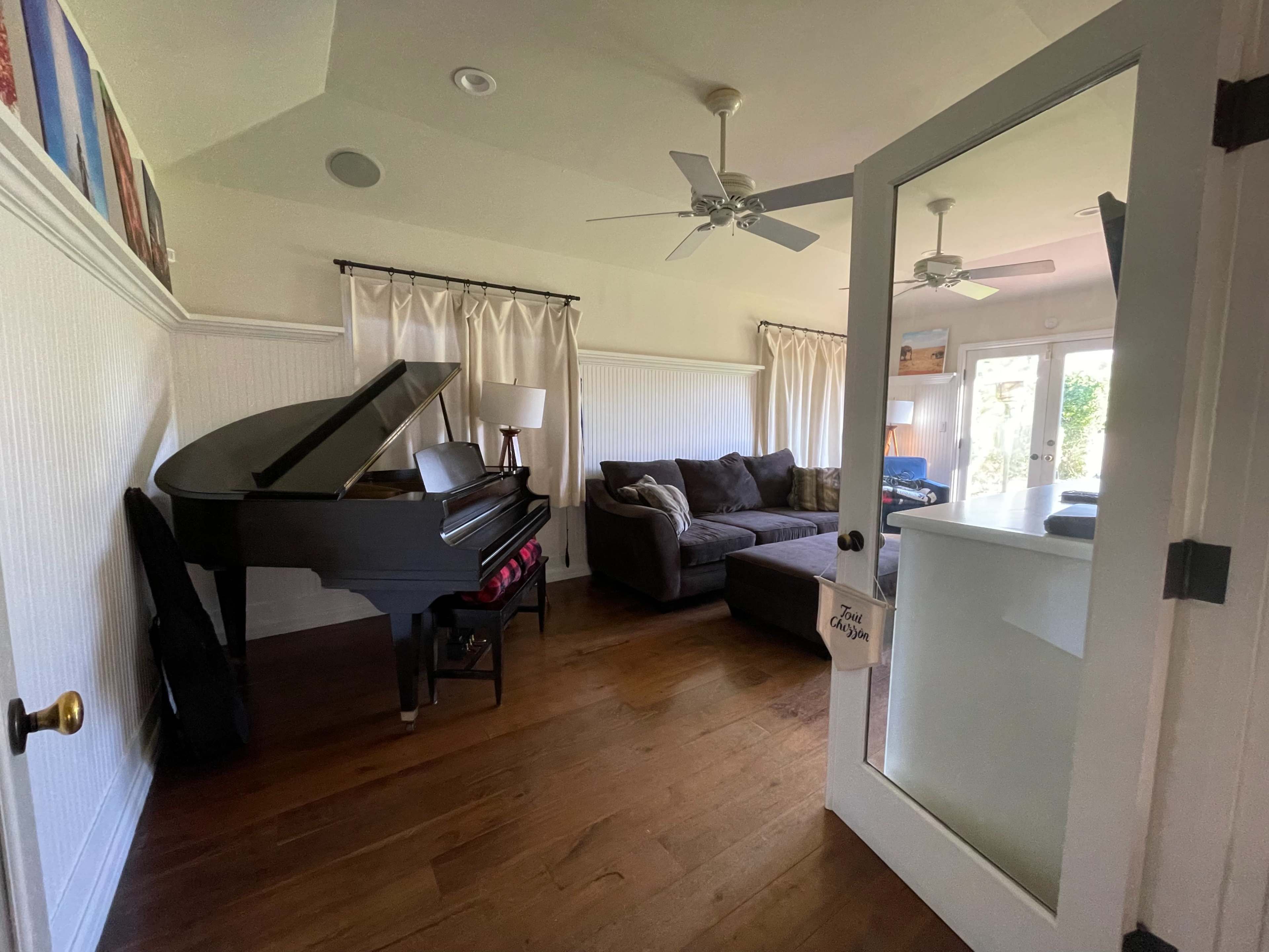 A living room with a piano, a dark sectional sofa, and large windows allowing natural light.
