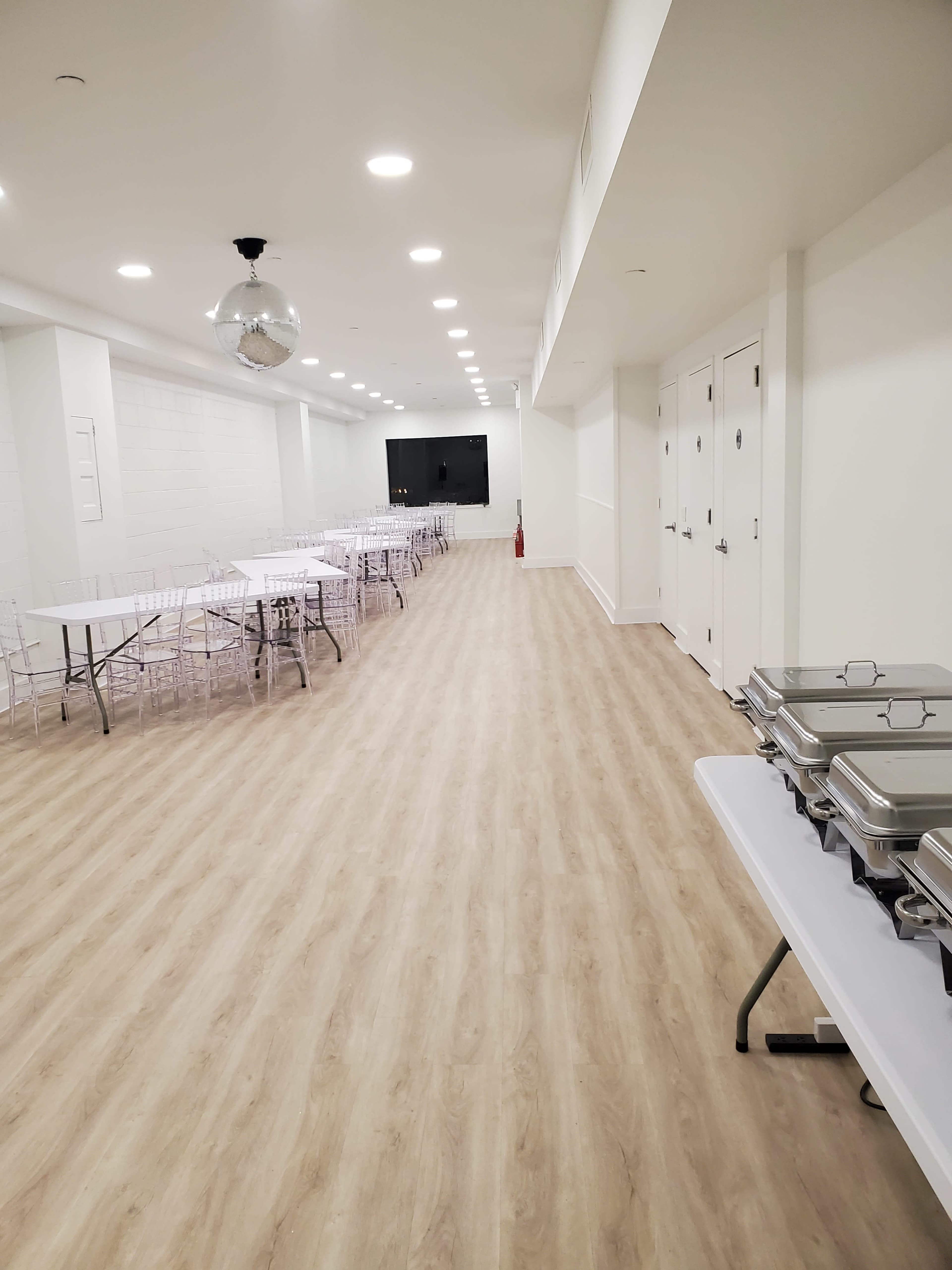 A large, well-lit event space features rows of tables and chairs along with a buffet setup on one side.