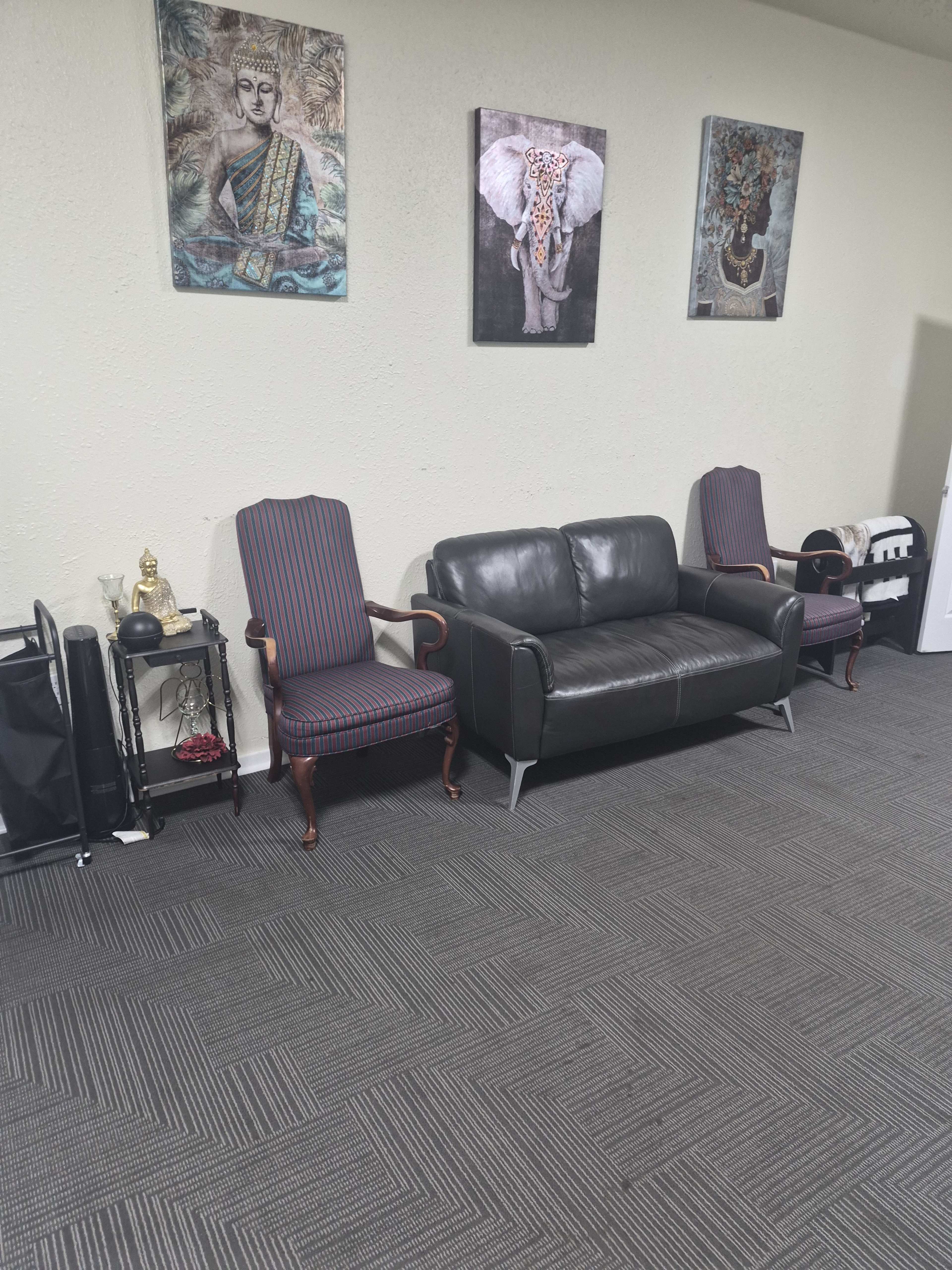 The image shows a waiting area with a black leather sofa and two armchairs against a wall adorned with three framed artworks.