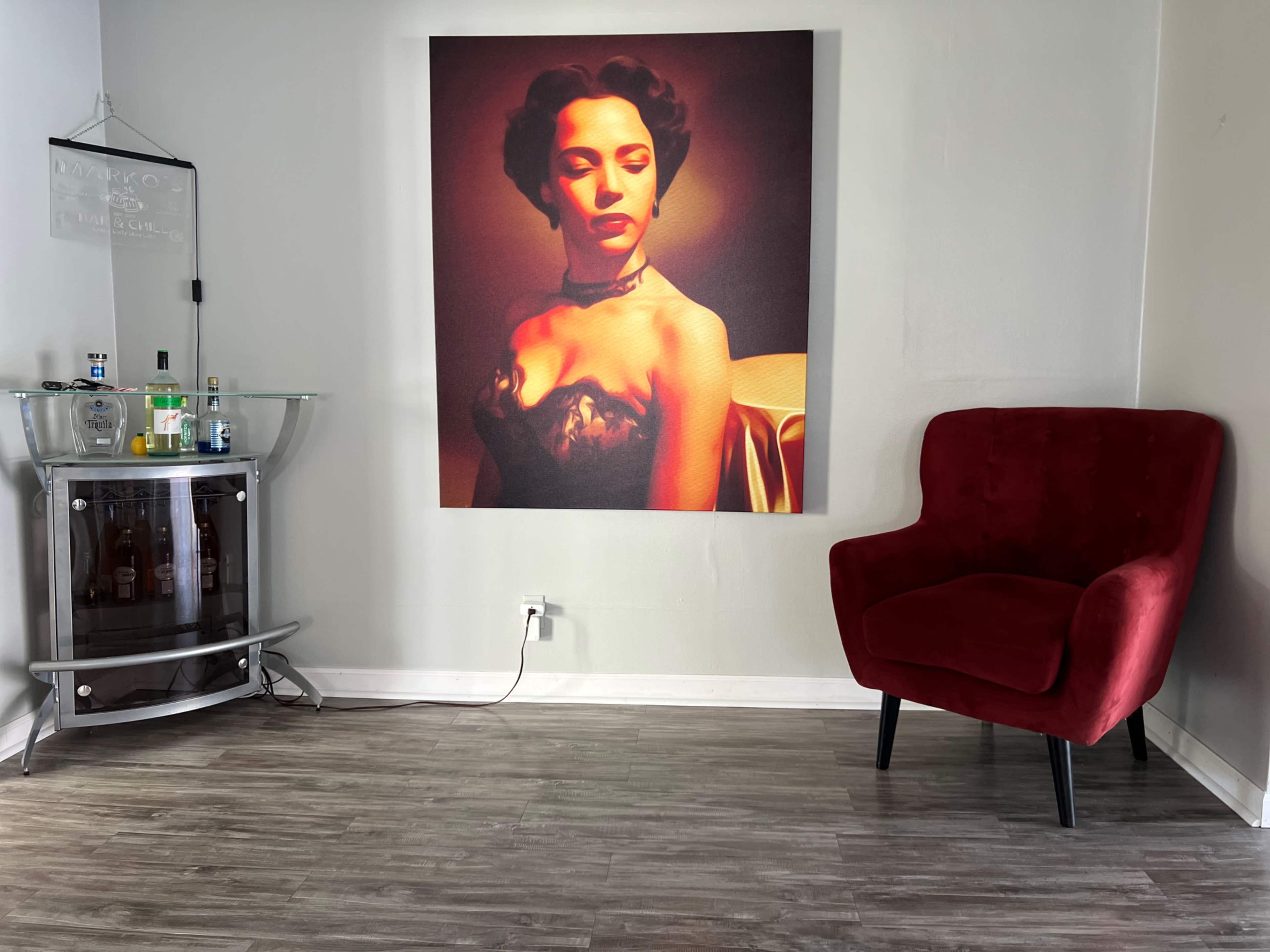 The scene features a red chair beside a glass bar cart displaying various bottles, with a large portrait of a woman in a dramatic pose hanging on the wall.