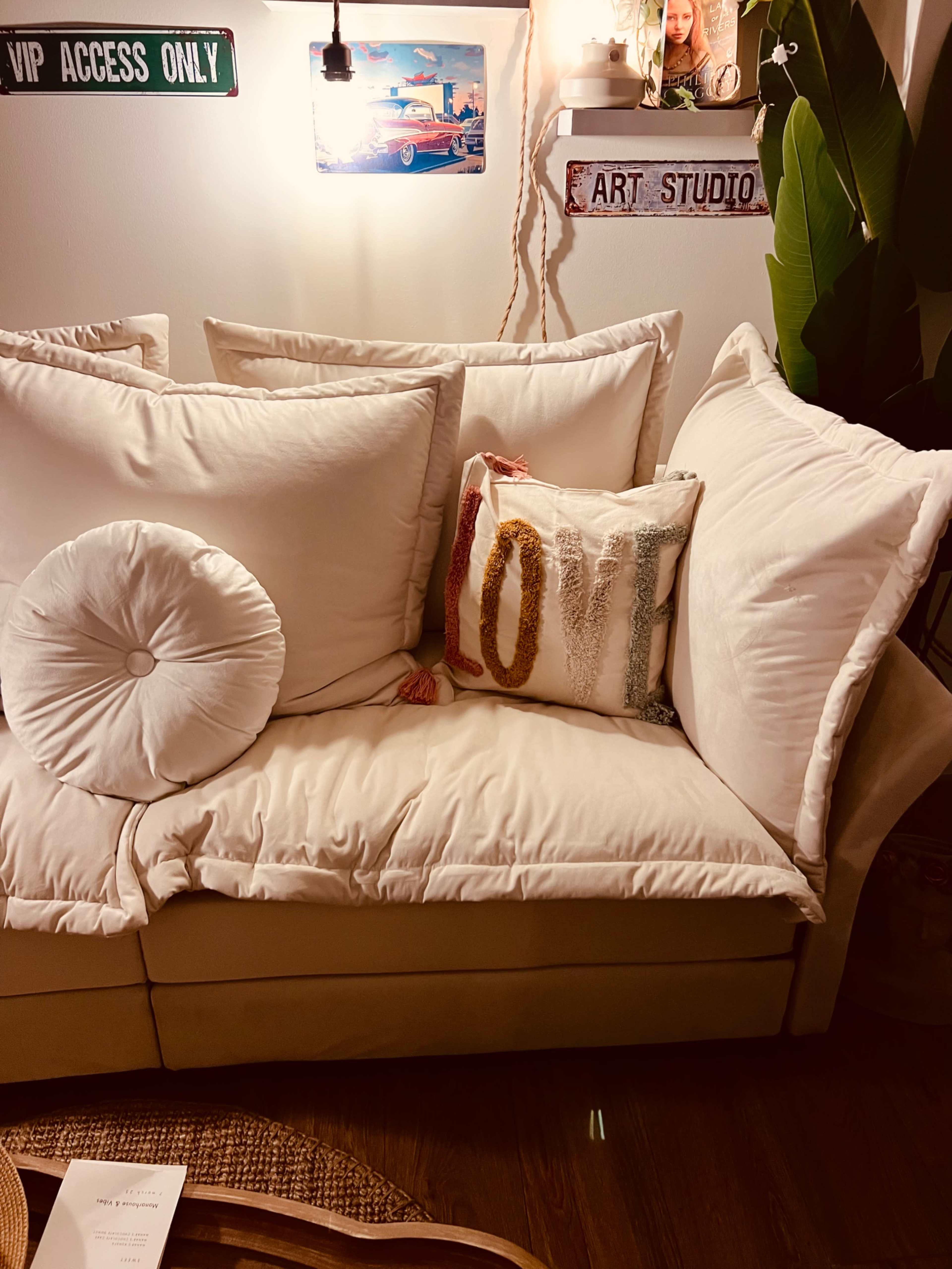 A cozy white couch adorned with large pillows and a decorative "LOVE" pillow is set against a softly lit wall.
