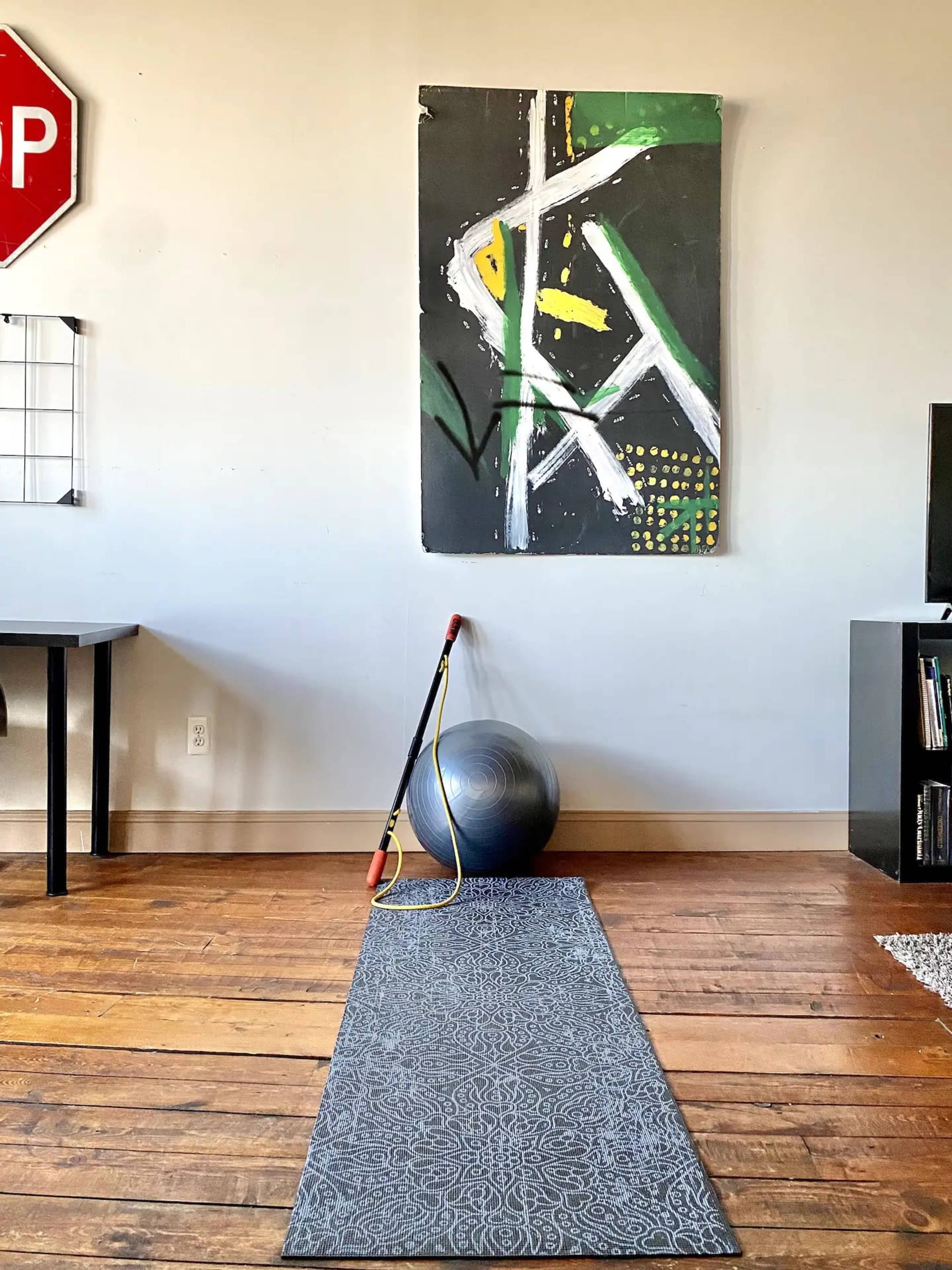 A fitness area with a yoga mat, an exercise ball, a resistance band, and a piece of abstract artwork on the wall.
