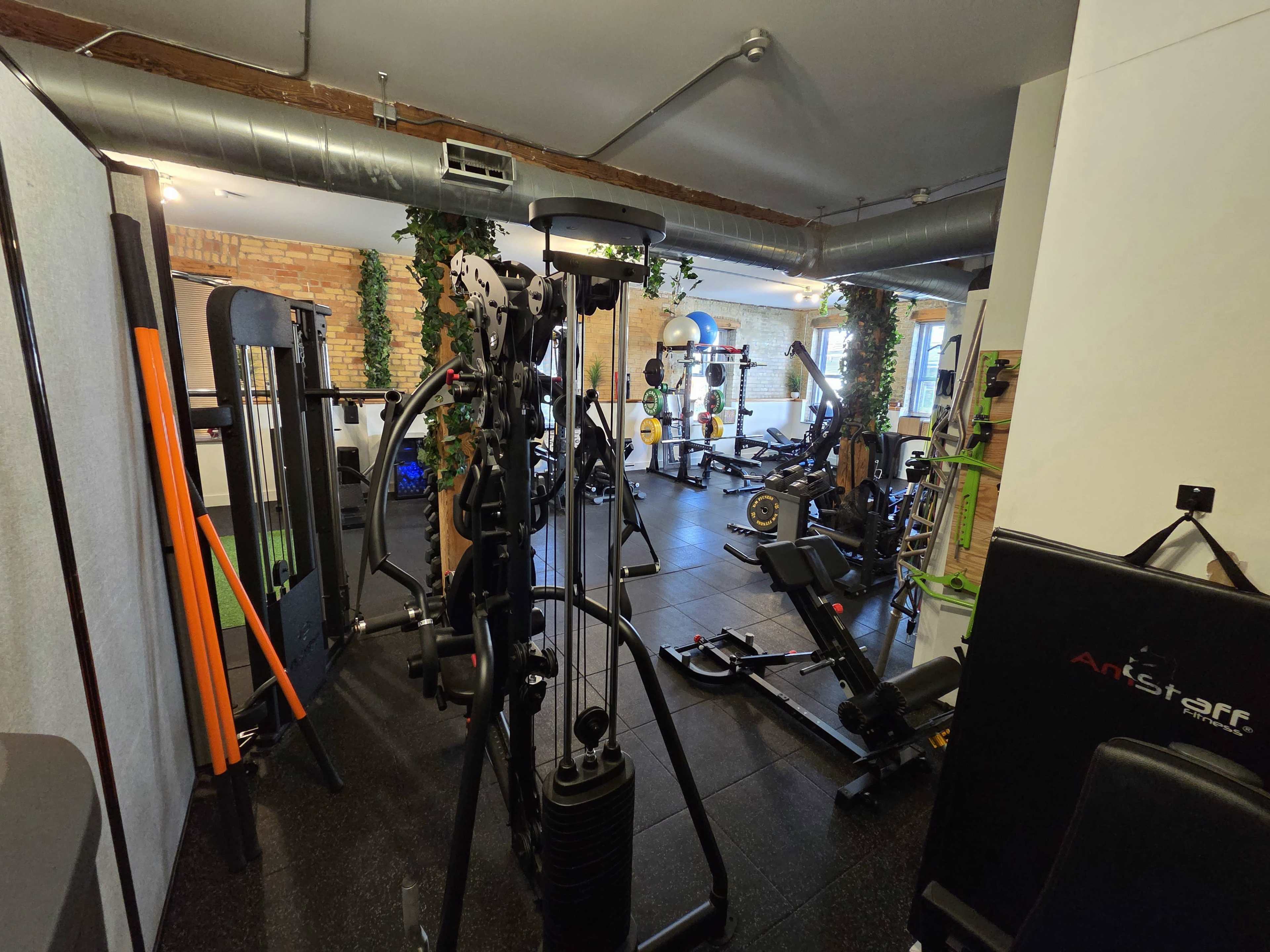 The image shows a well-equipped gym featuring various strength training machines and workout equipment arranged in a spacious, well-lit environment.
