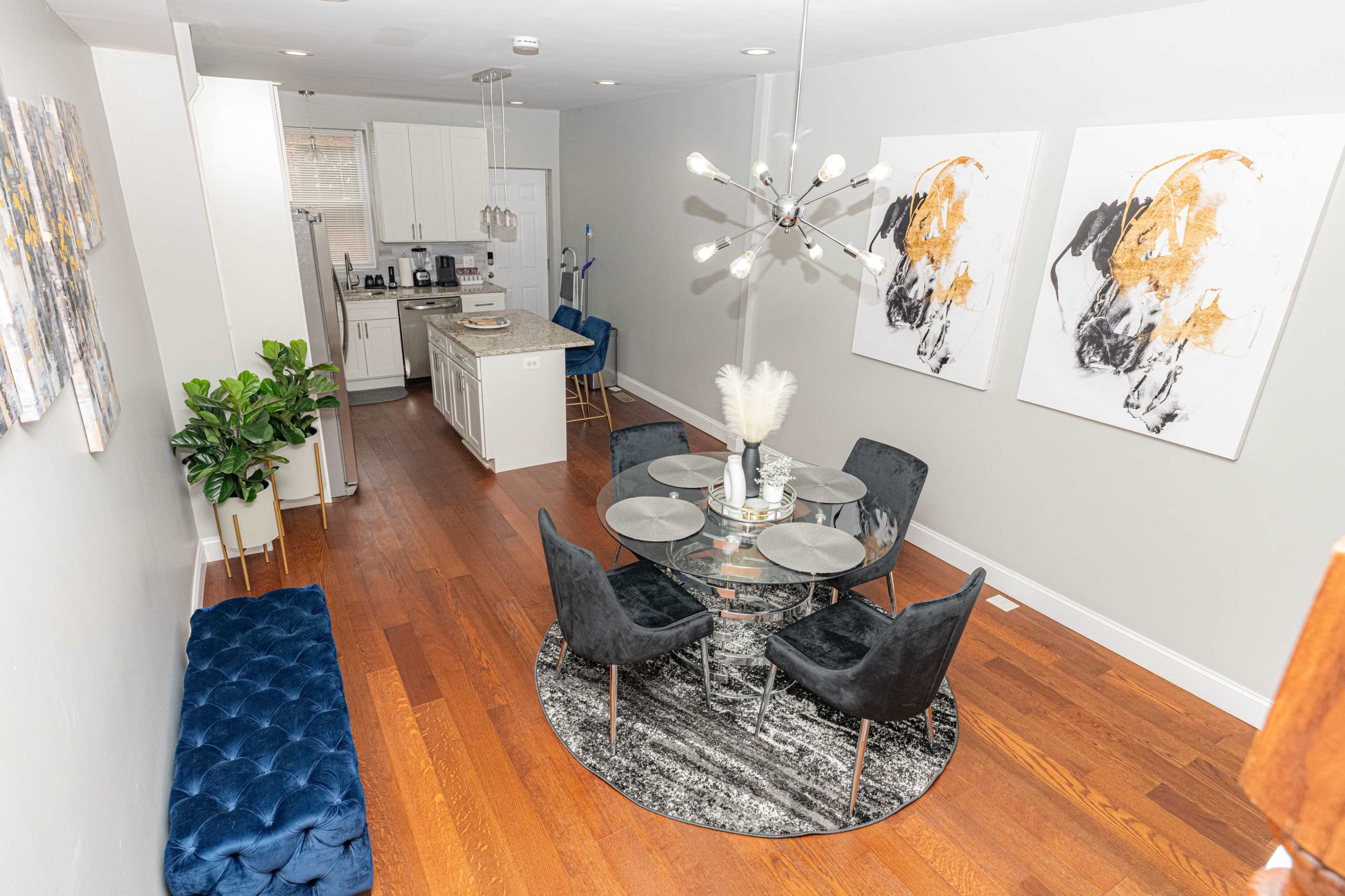 A modern dining area features a round glass table surrounded by black upholstered chairs, with abstract artworks on the walls and hardwood flooring.