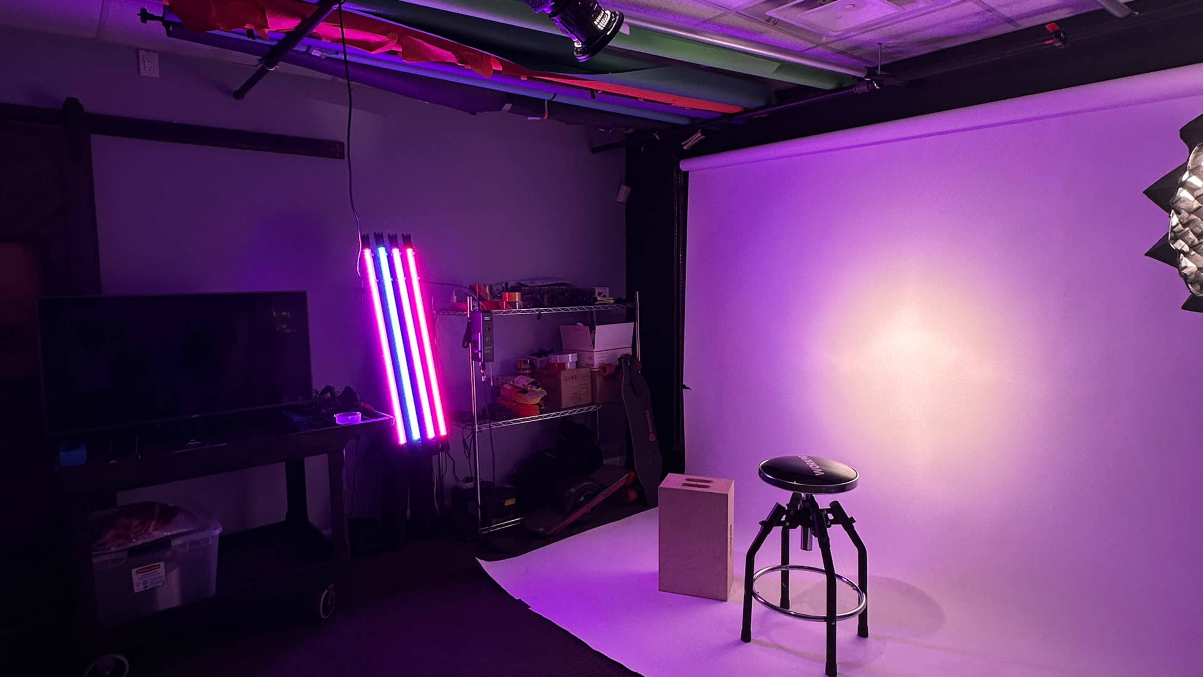 A photography studio with a white backdrop, a stool, a box, and colorful lighting.