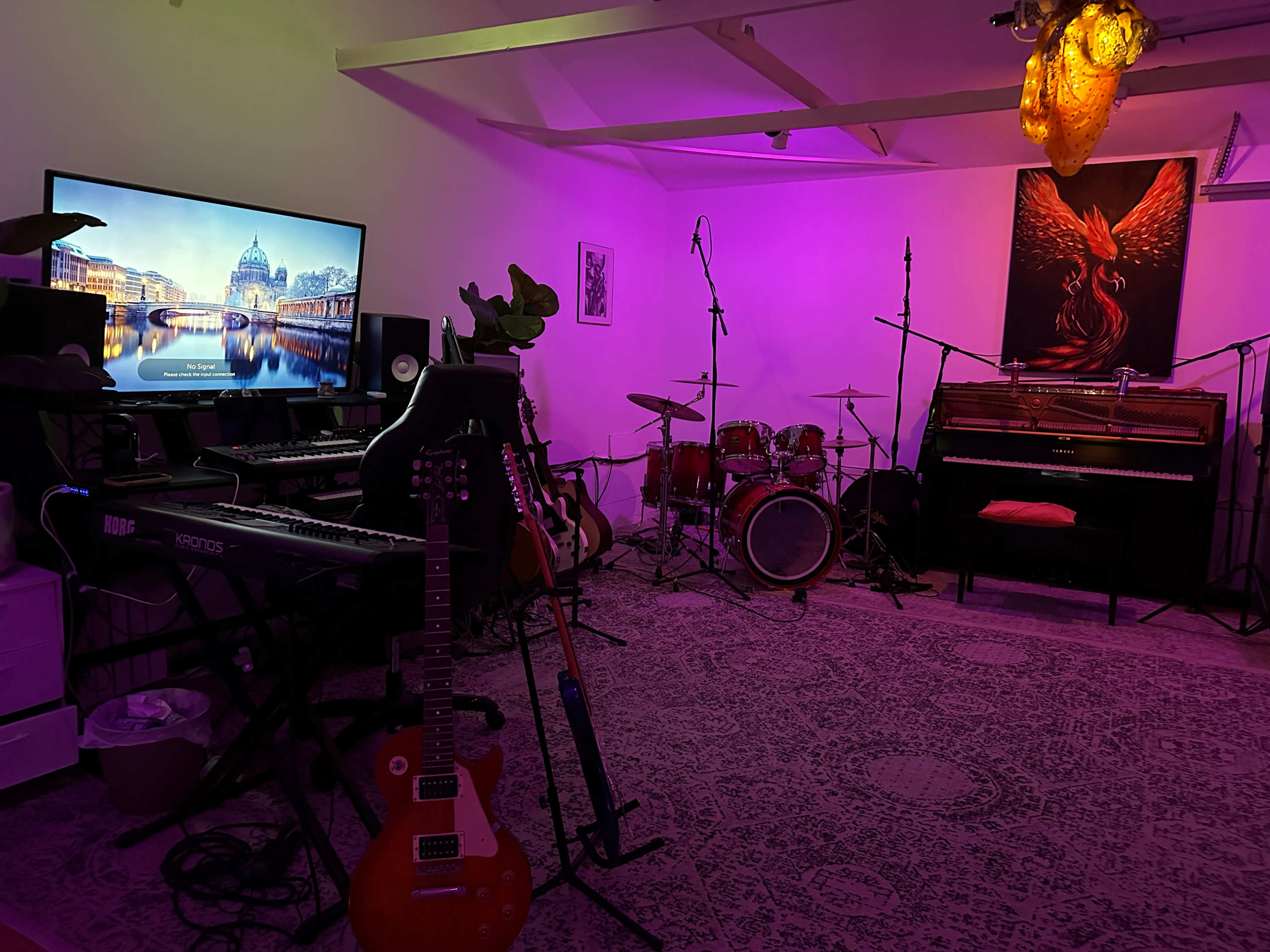 The room features musical instruments including a guitar, keyboard, drums, and a piano, alongside colorful lighting and a large television displaying an image.