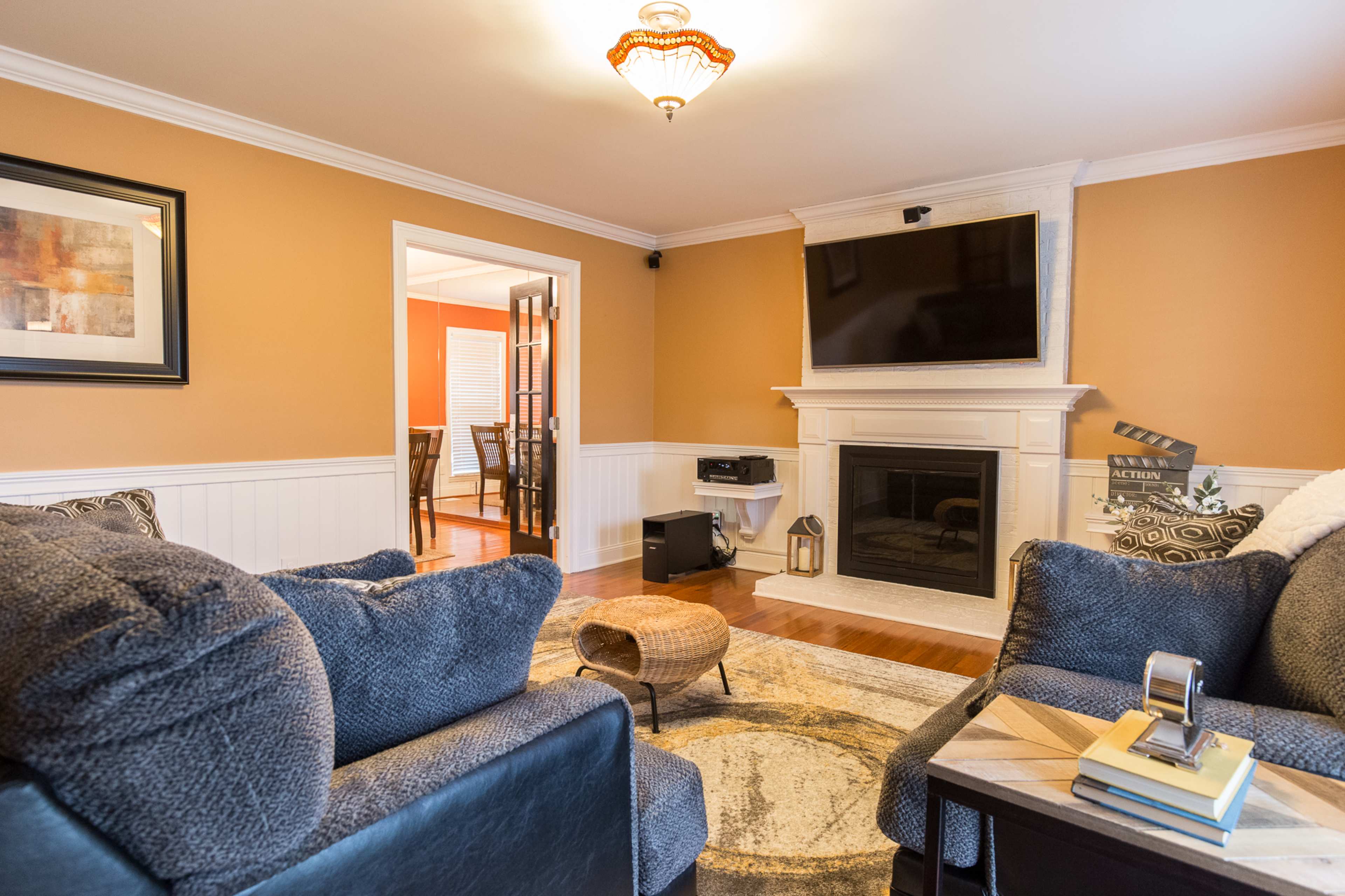 A cozy living room features two dark sofas, a fireplace with a mounted television above it, and an entrance to a dining area in the background.