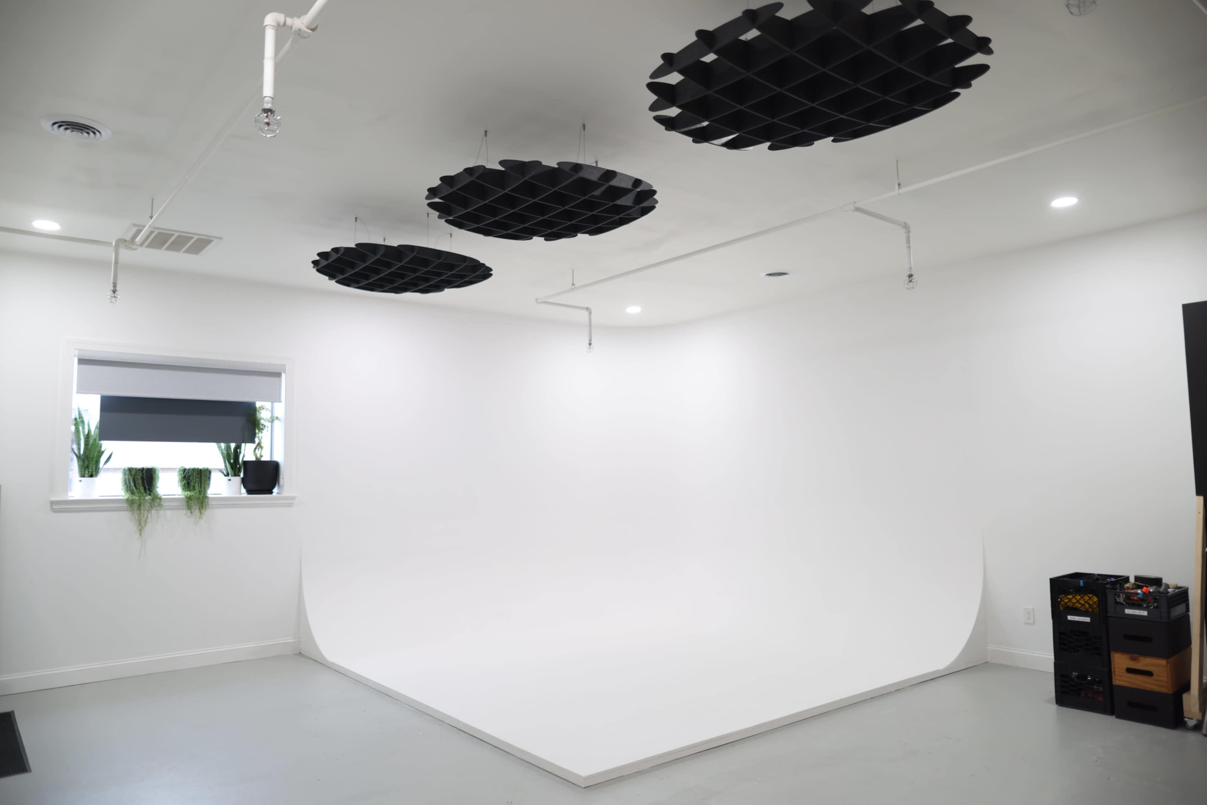 A spacious photography studio with a seamless white backdrop, a plain gray floor, and acoustic panels suspended from the ceiling.