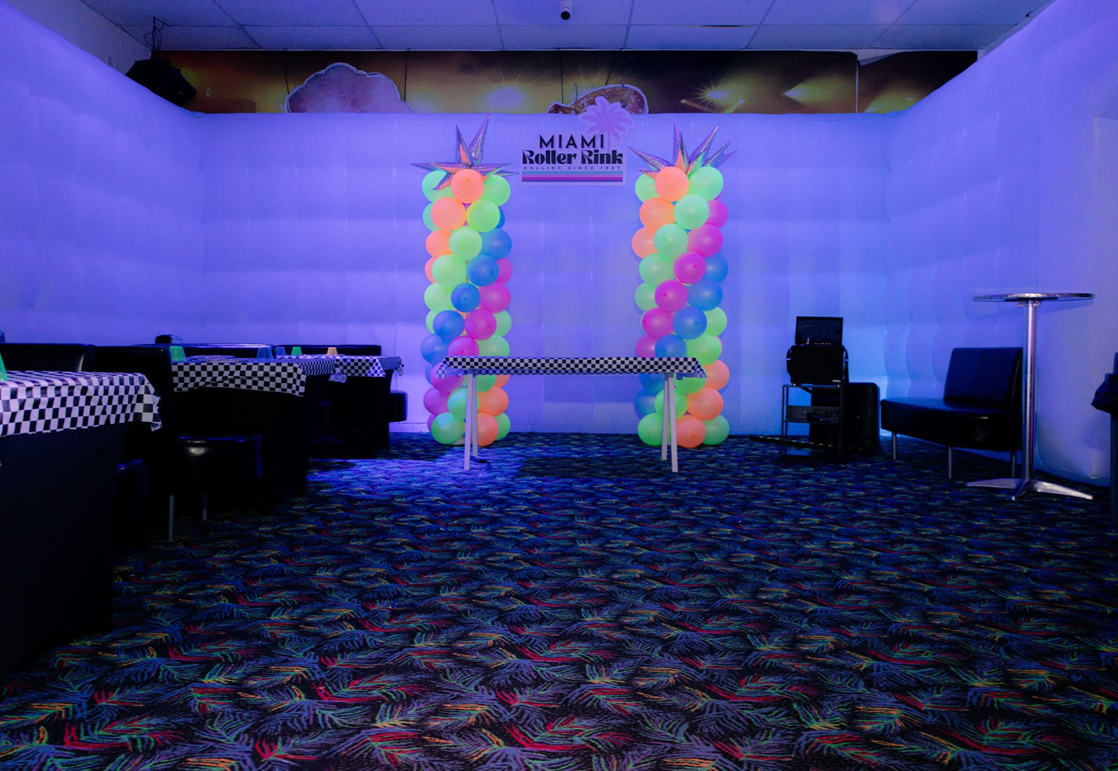 The image shows the interior of a roller skating rink decorated with colorful balloons and a checkerboard table in a brightly lit room.