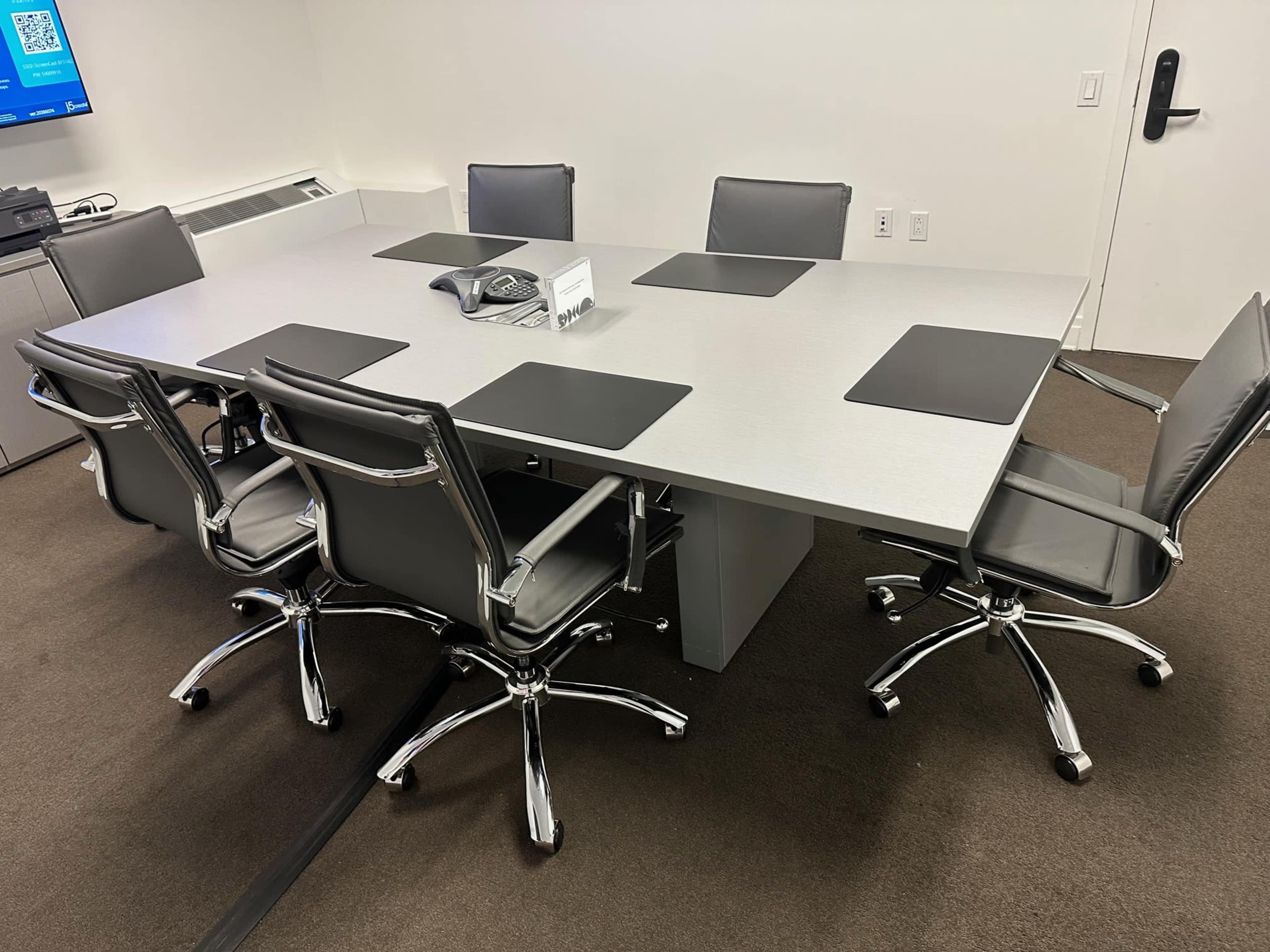A modern conference room features a large metallic table surrounded by six ergonomic chairs.