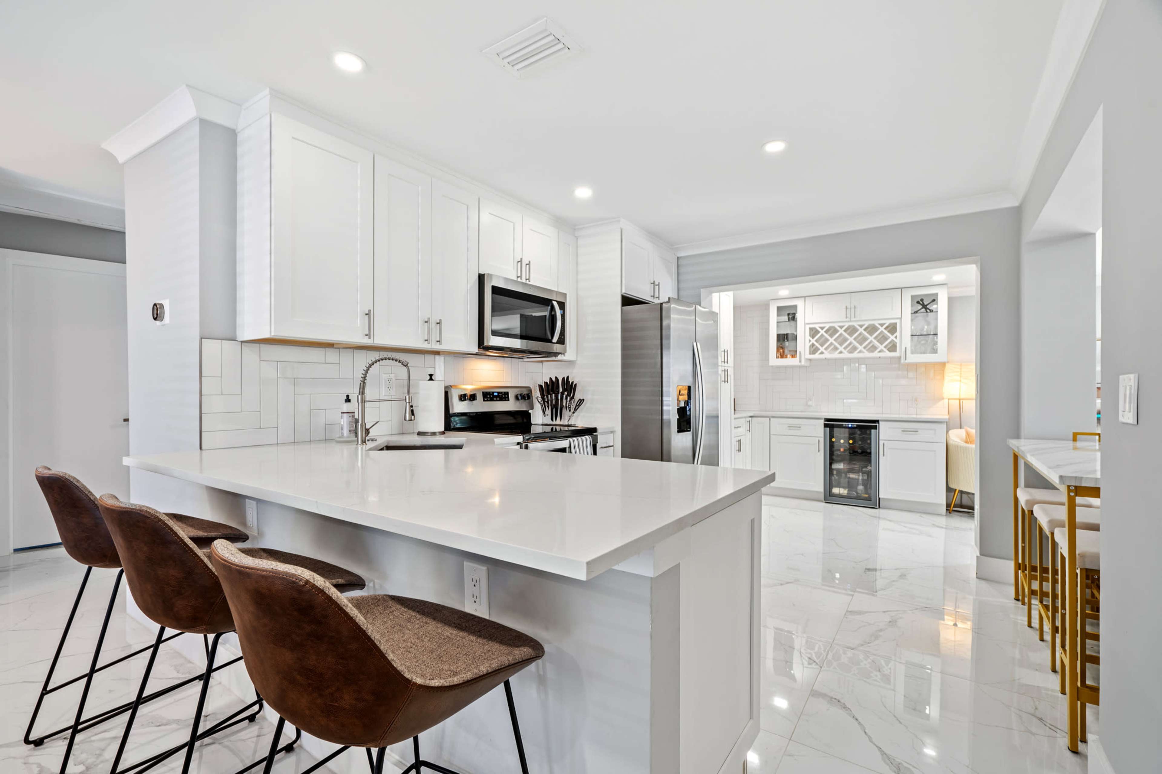 A modern kitchen features white cabinetry, stainless steel appliances, and a large island with bar seating.