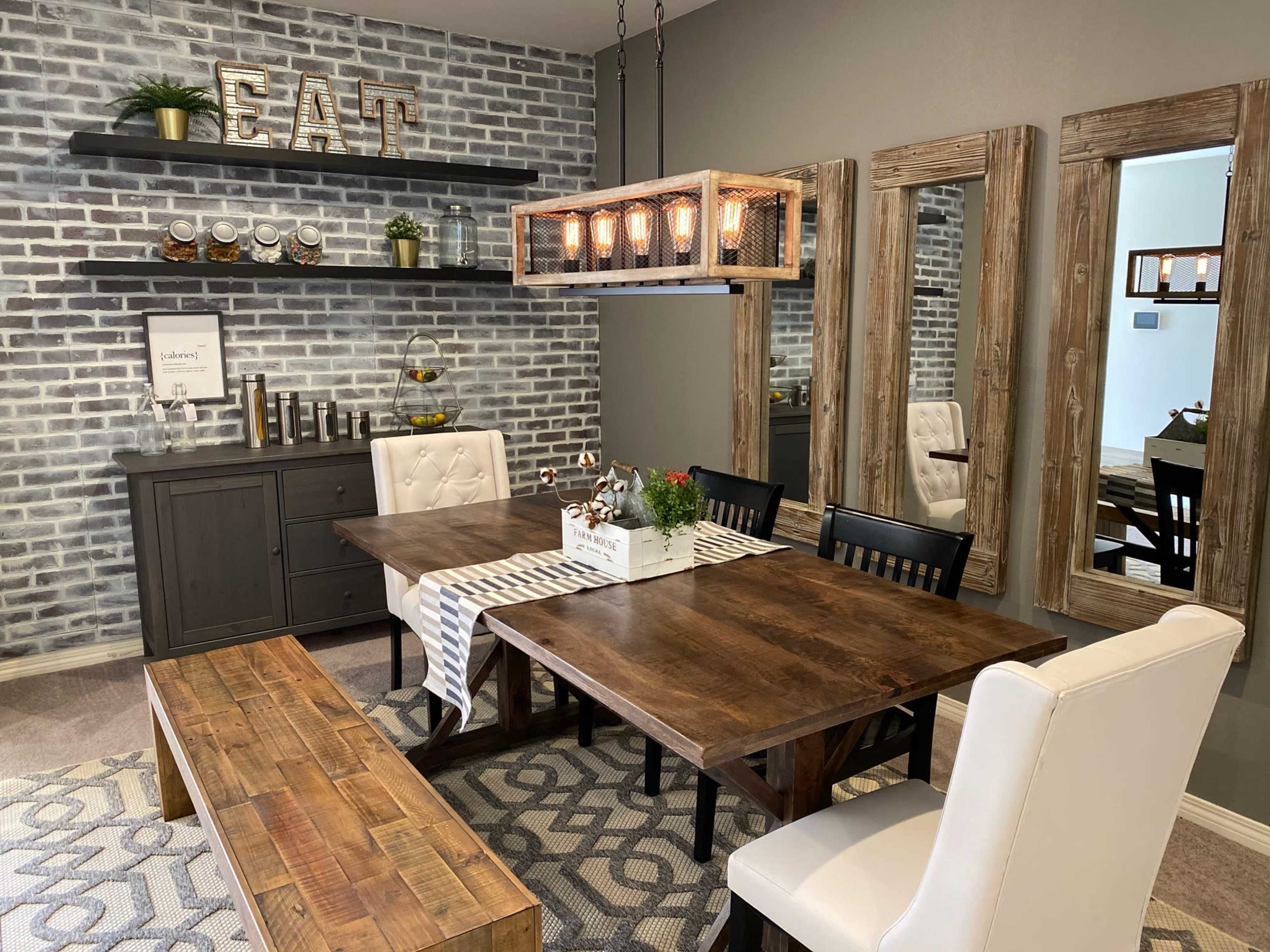 A dining area with a wooden table surrounded by black and white chairs, set against a backdrop of brick-patterned walls and decorative shelves.