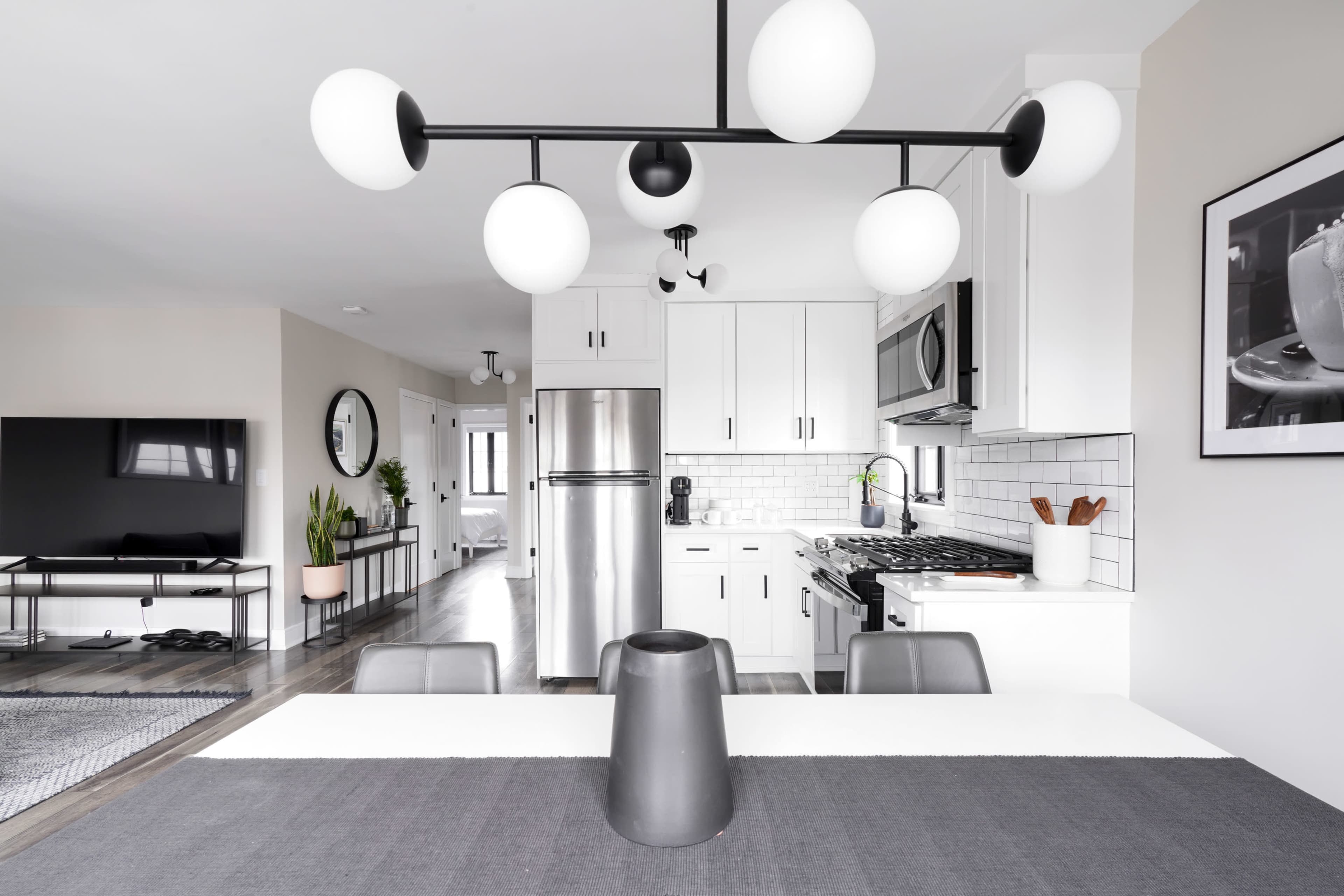 A modern kitchen features white cabinets, stainless steel appliances, and a black and white decor scheme, with a dining table centered under a geometric light fixture.
