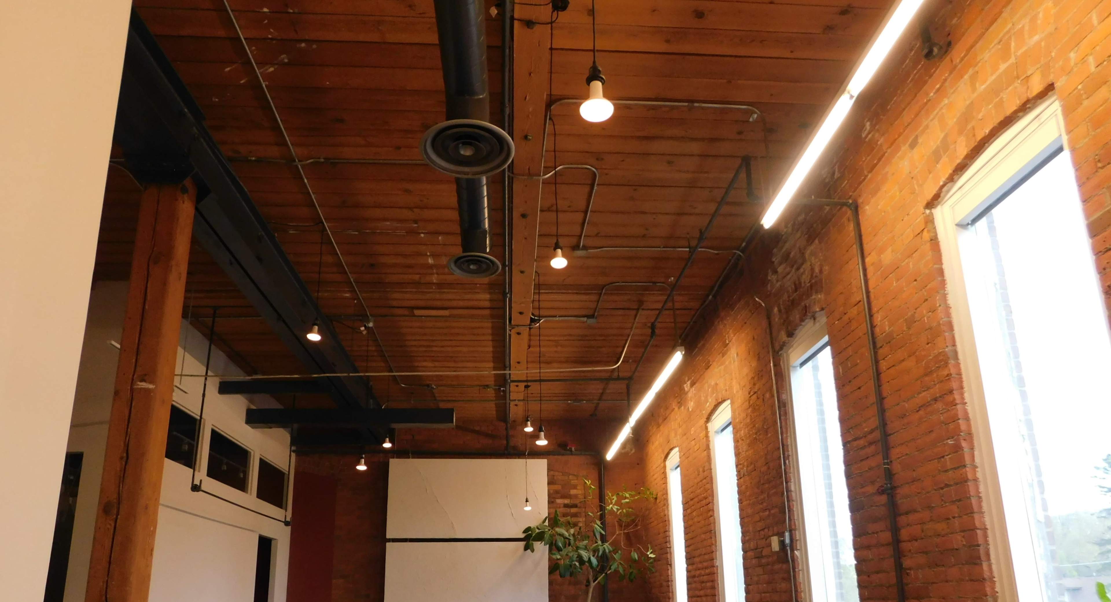 A room with exposed brick walls, wooden beams, and various light fixtures along the ceiling.
