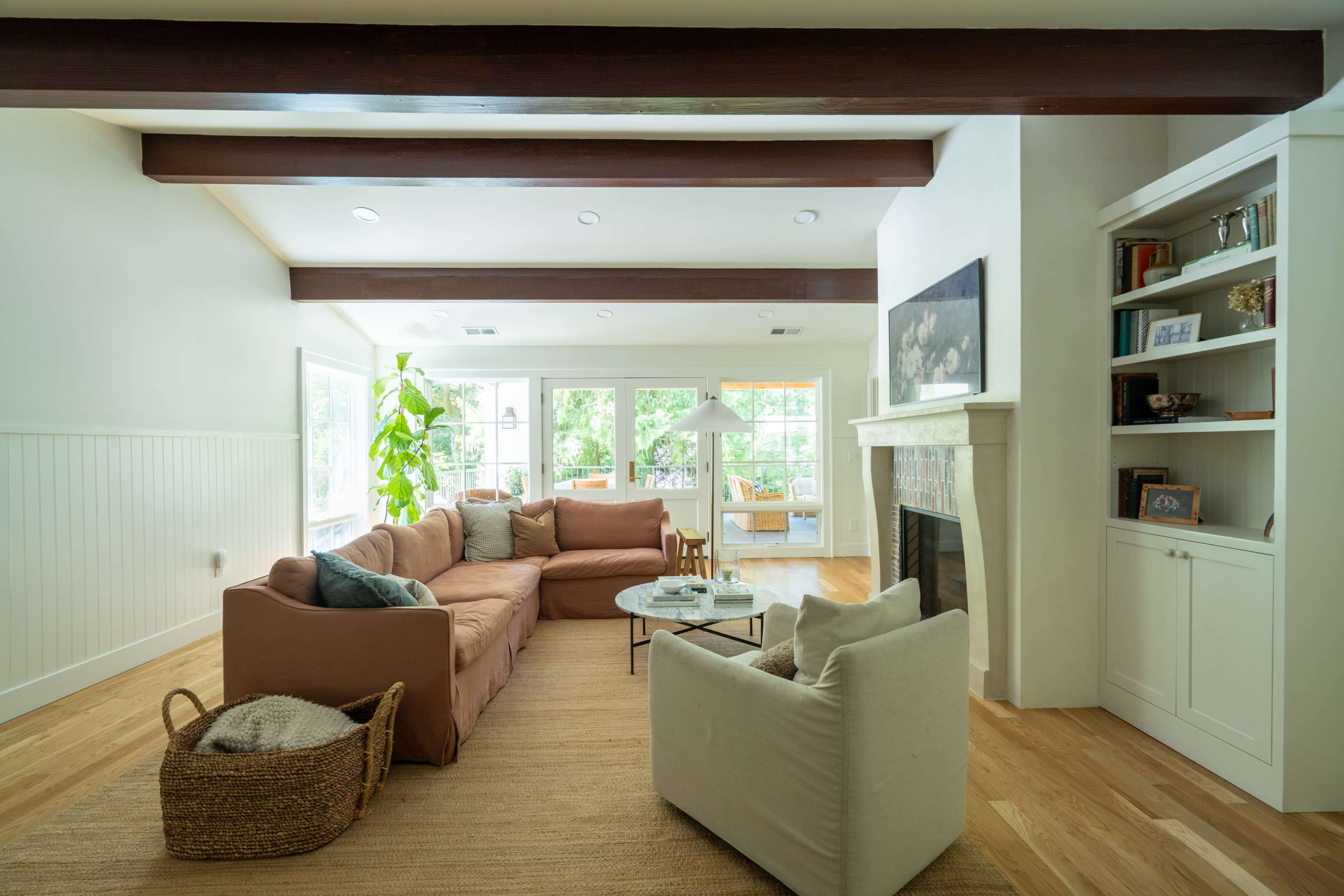 A spacious living room features a large sectional sofa, a coffee table, and a fireplace, with natural light streaming through large windows.