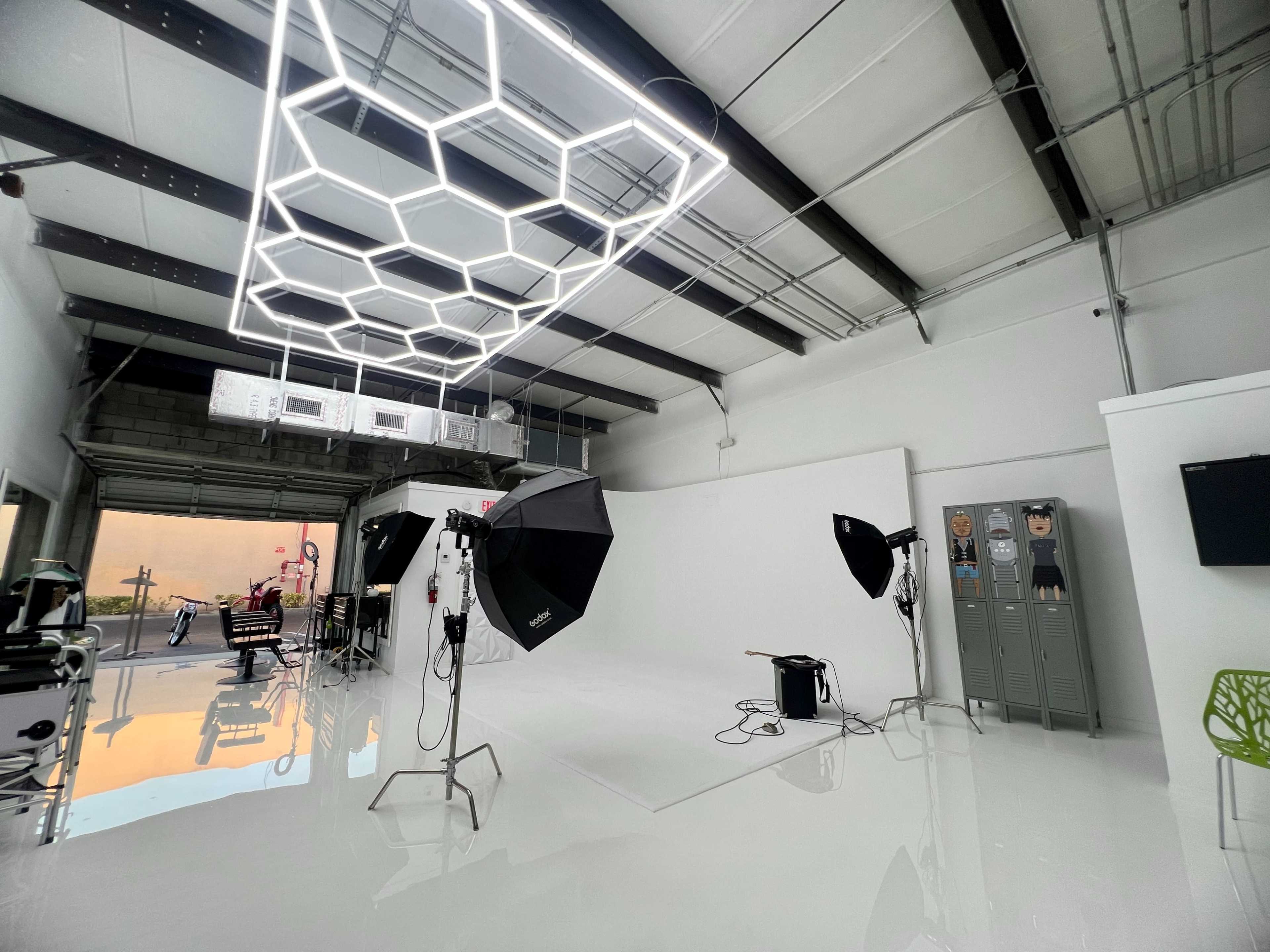A modern photography studio with a white backdrop, lighting equipment, and a sleek honeycomb-patterned ceiling fixture.