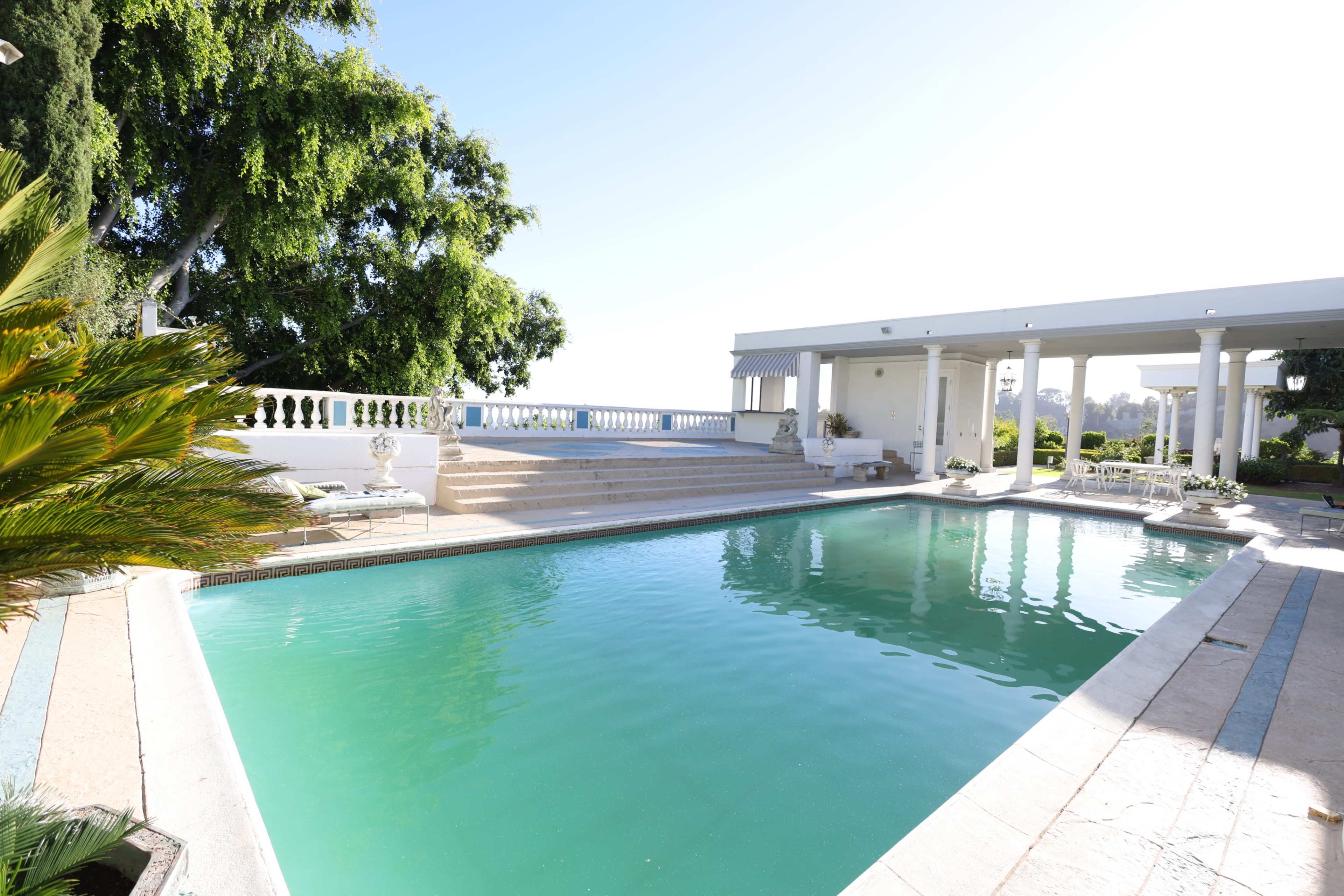 A landscaped swimming pool surrounded by steps, palm trees, and a modern pavilion.