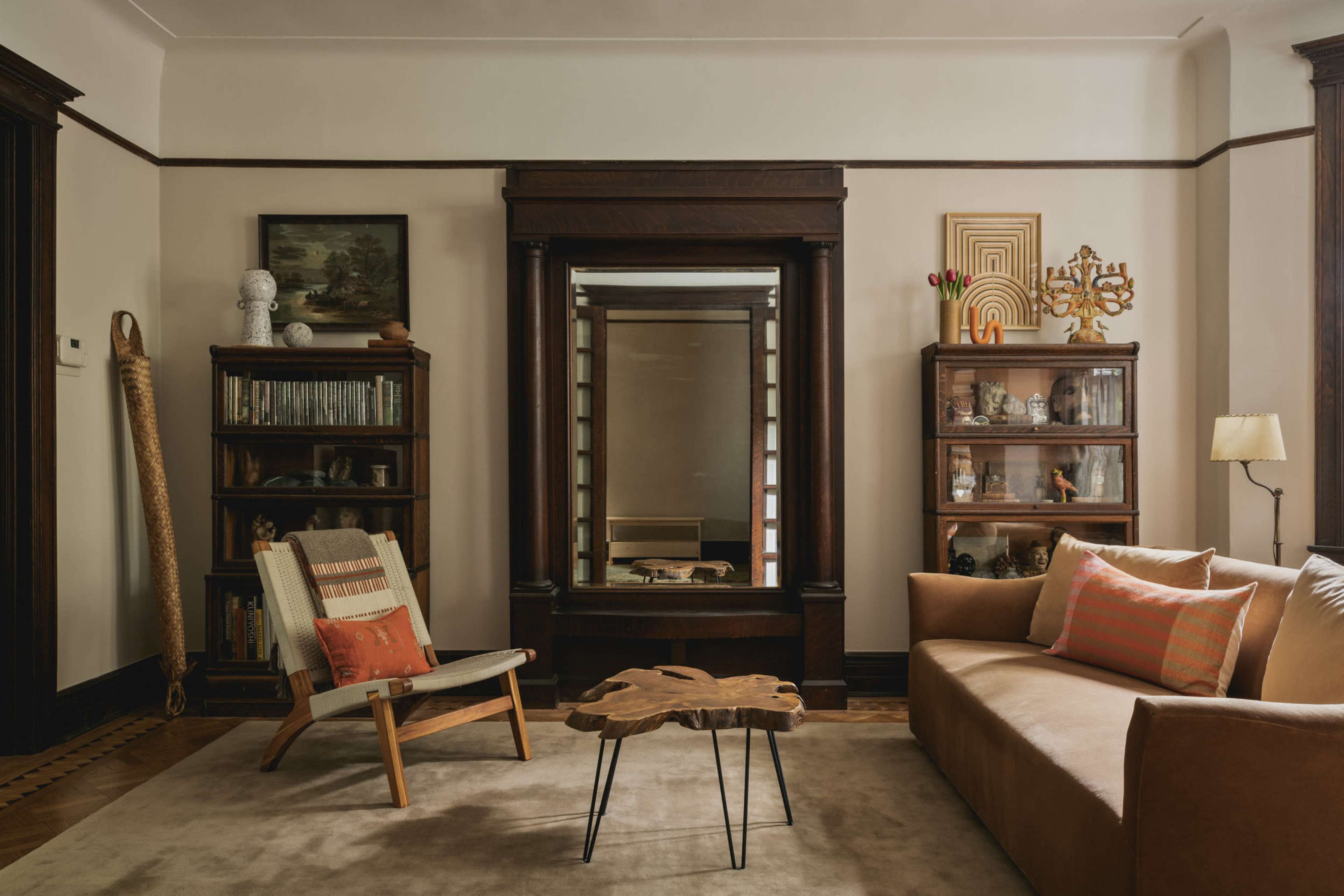 A cozy living room features a beige sofa, a wooden coffee table, bookshelves filled with various items, and a mirror reflecting the space.