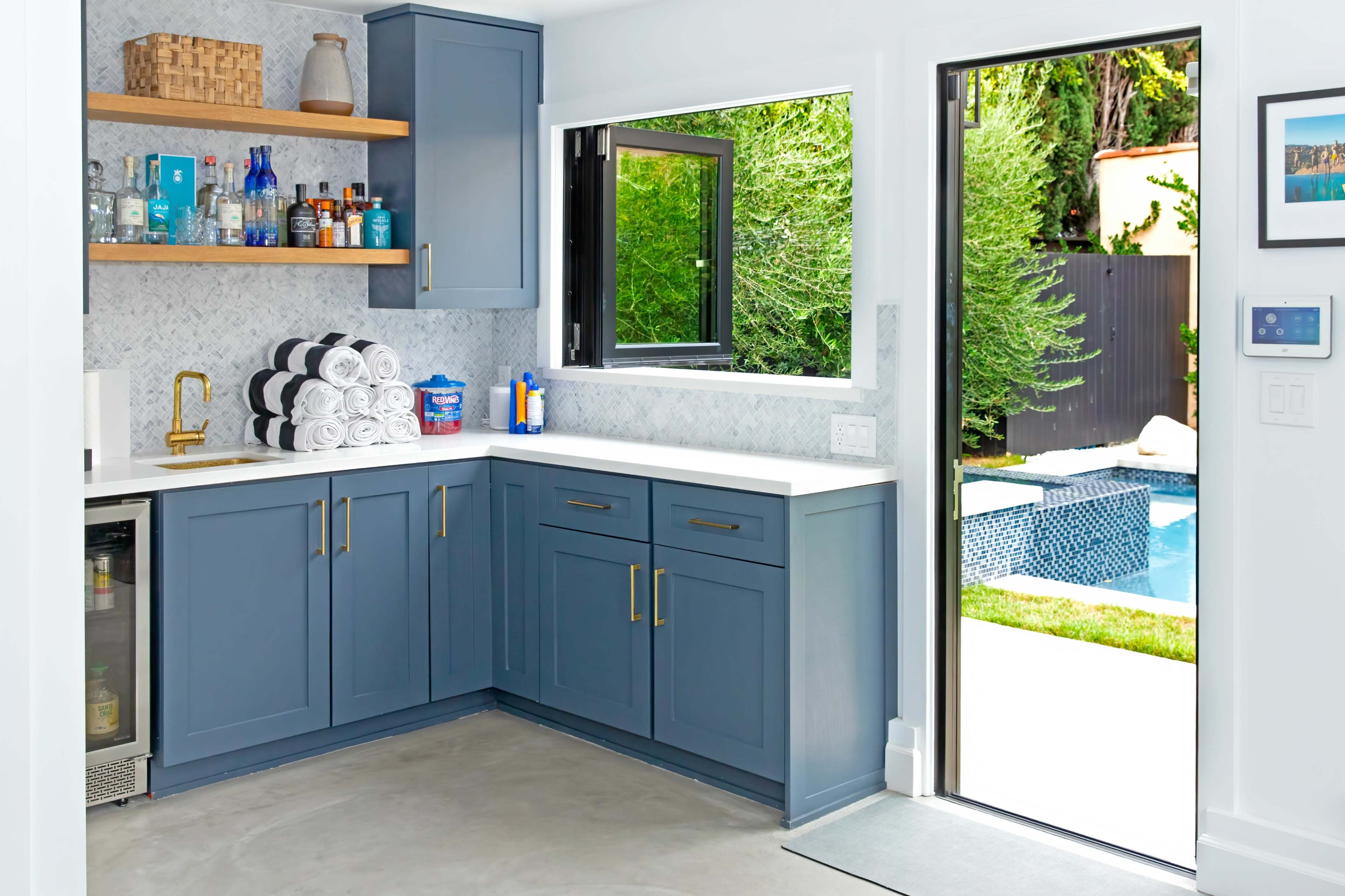 A modern kitchen with blue cabinets, a countertop, and a view of a pool area through an open door.