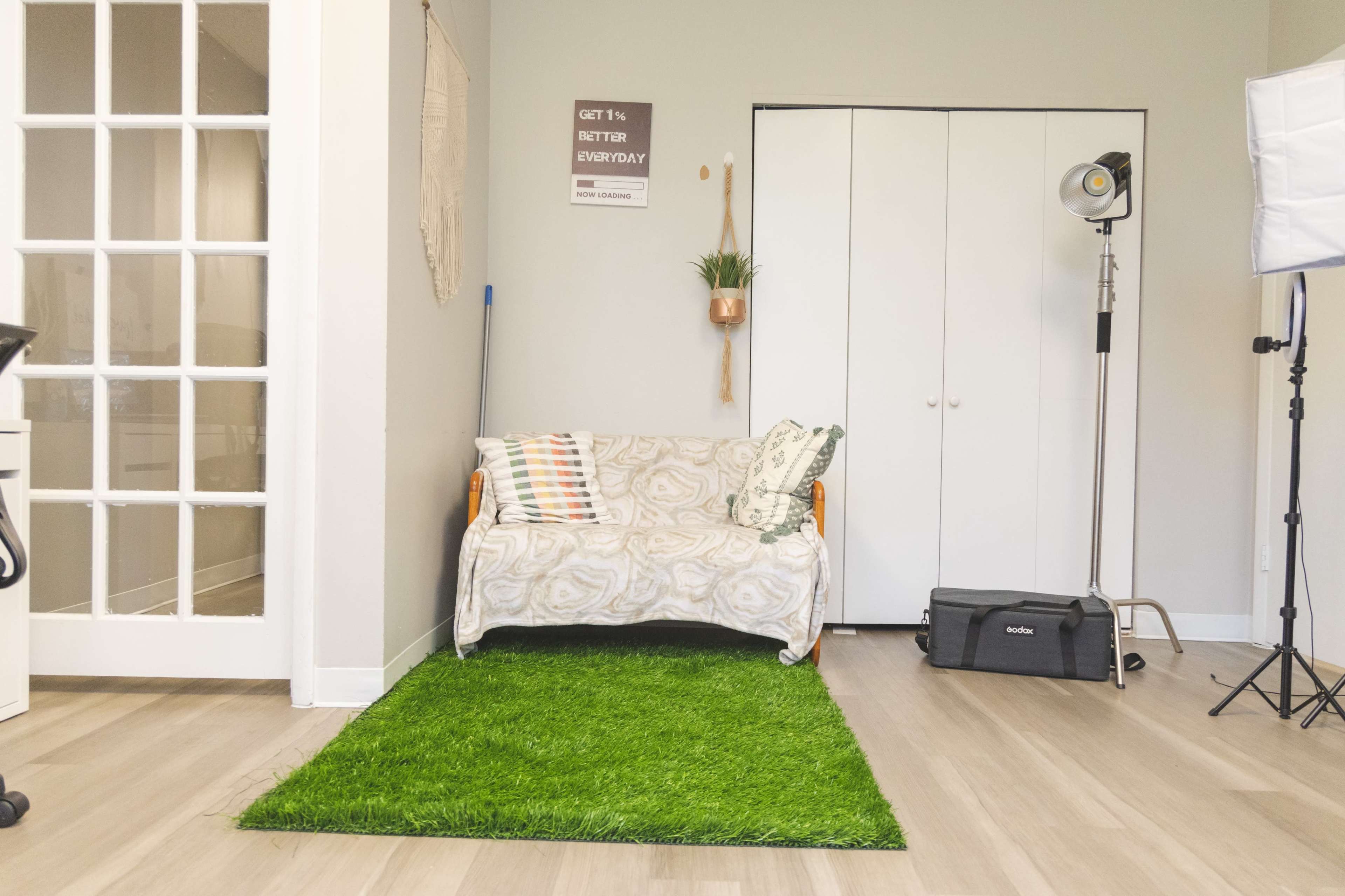 A minimalistic room featuring a couch covered with a patterned throw, a patch of artificial grass on the floor, and a closet in the background.