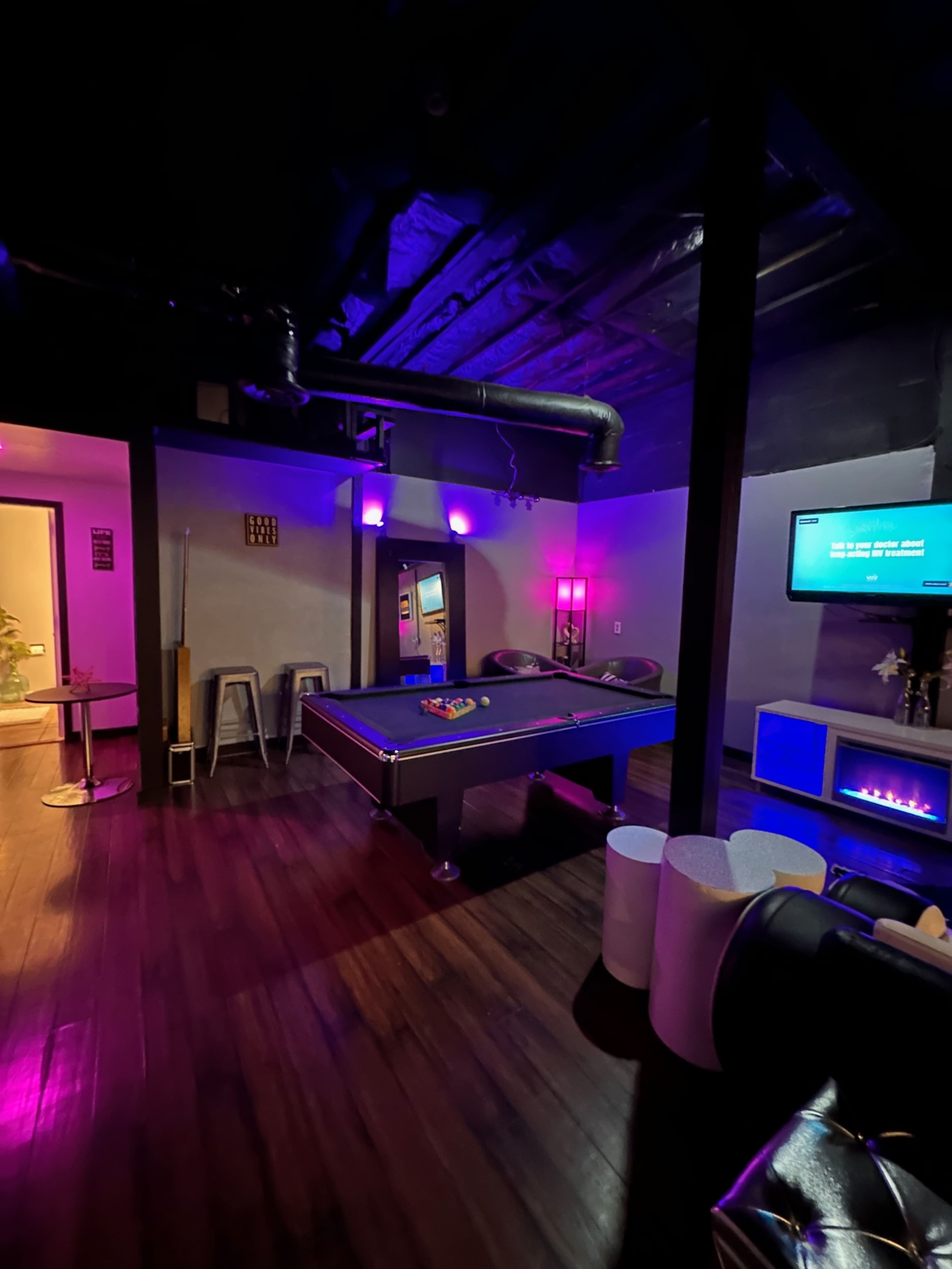 A billiards table is centered in a dimly lit room equipped with modern furniture and wall-mounted lighting.