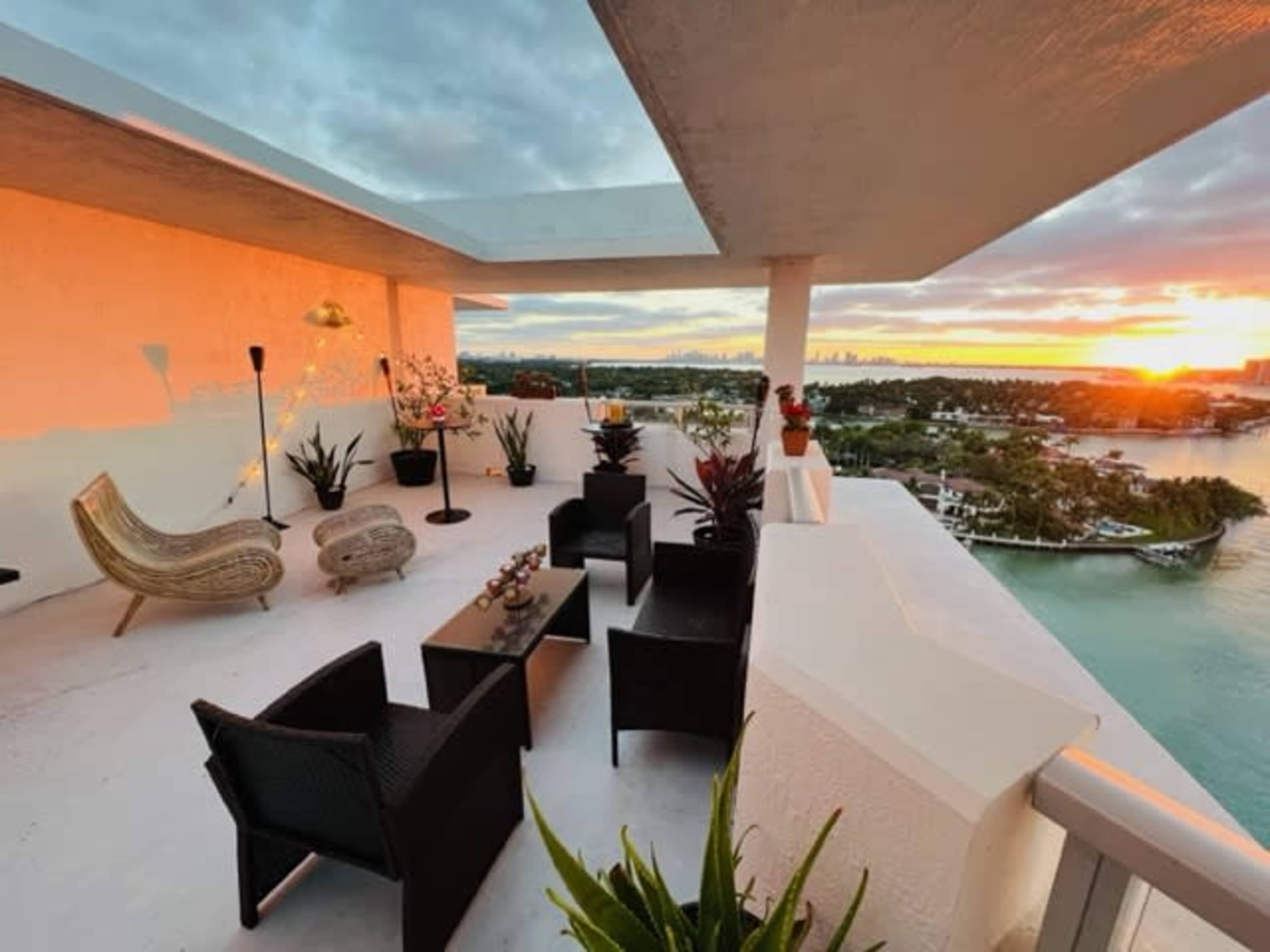 A terrace features modern seating and decorative plants overlooking a waterway at sunset.
