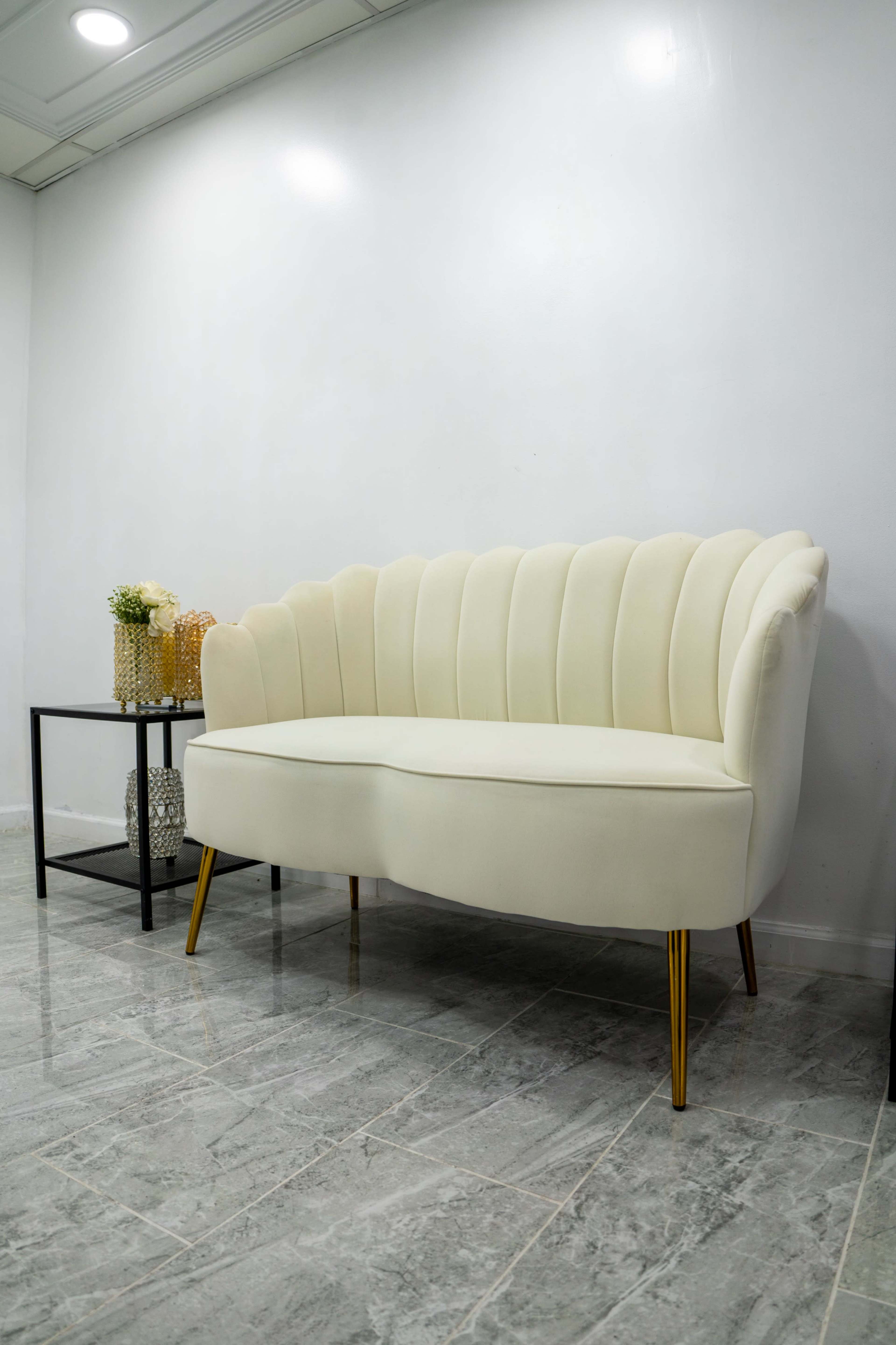 A cream-colored couch with a curved backrest sits against a white wall, accompanied by a small black side table with decorative items.