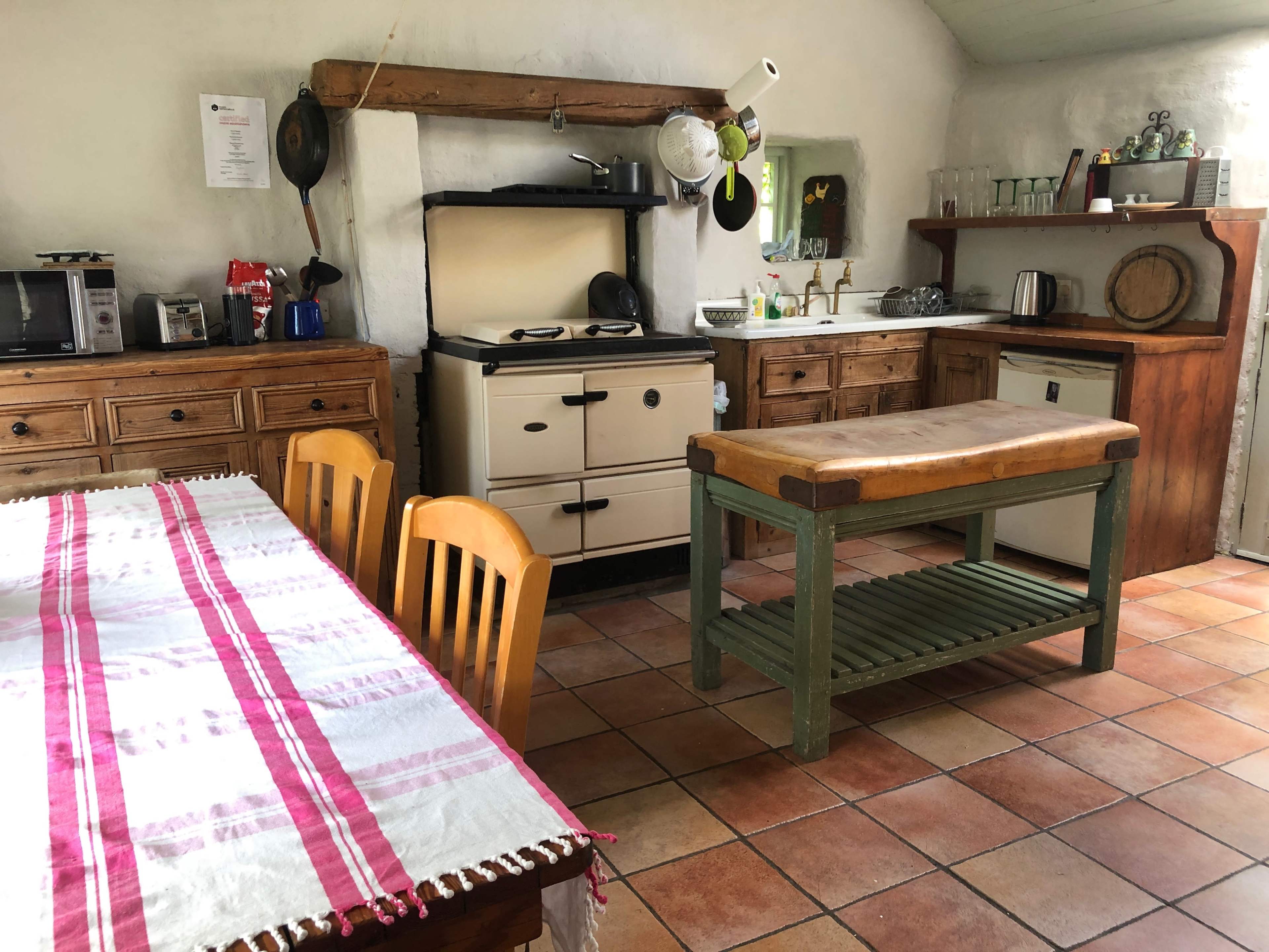 The image shows a rustic kitchen with wooden cabinets, a stove, and a dining table set with a checkered cloth.