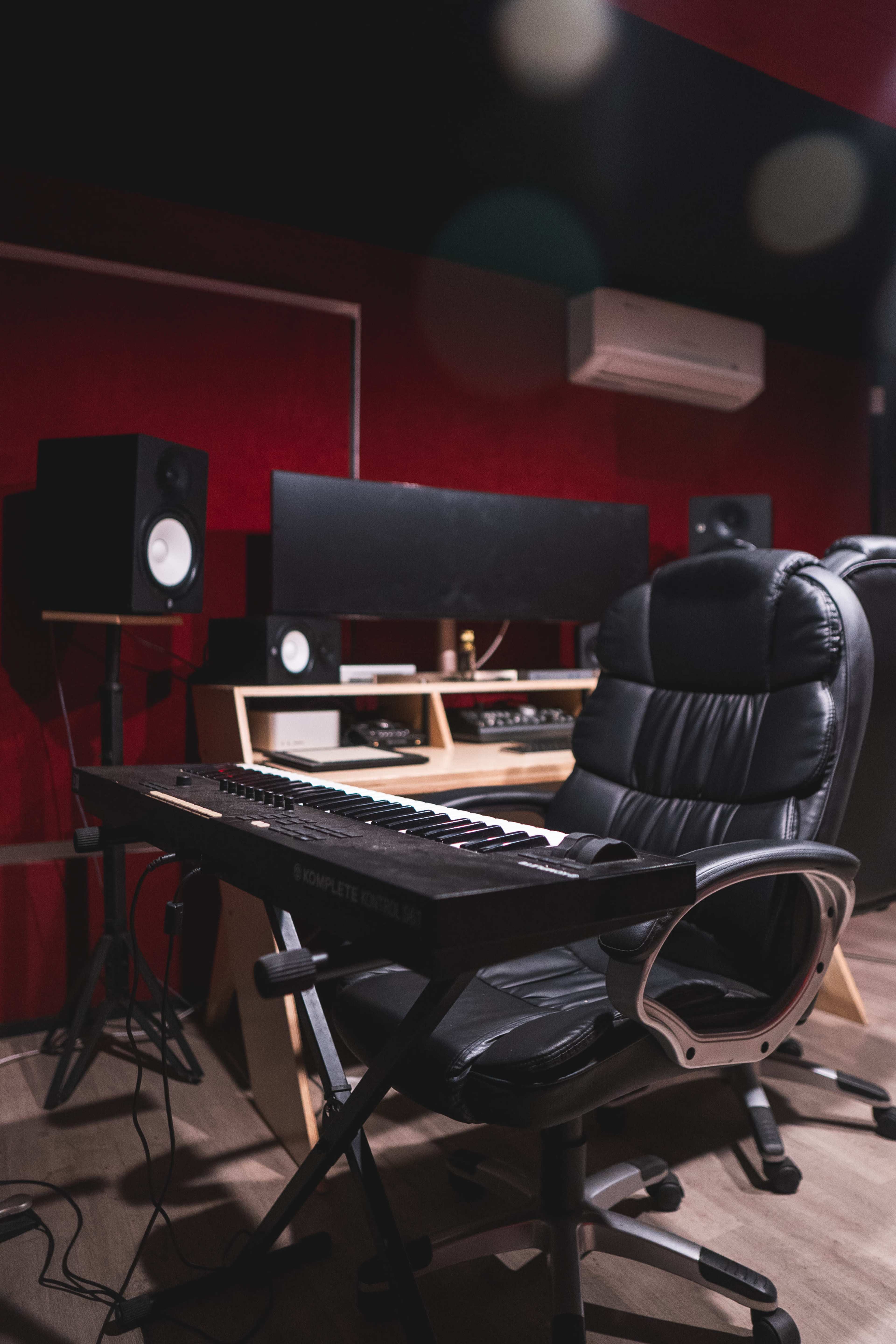 A black keyboard sits on a folding chair in a music studio with speakers and a mixing console visible in the background.