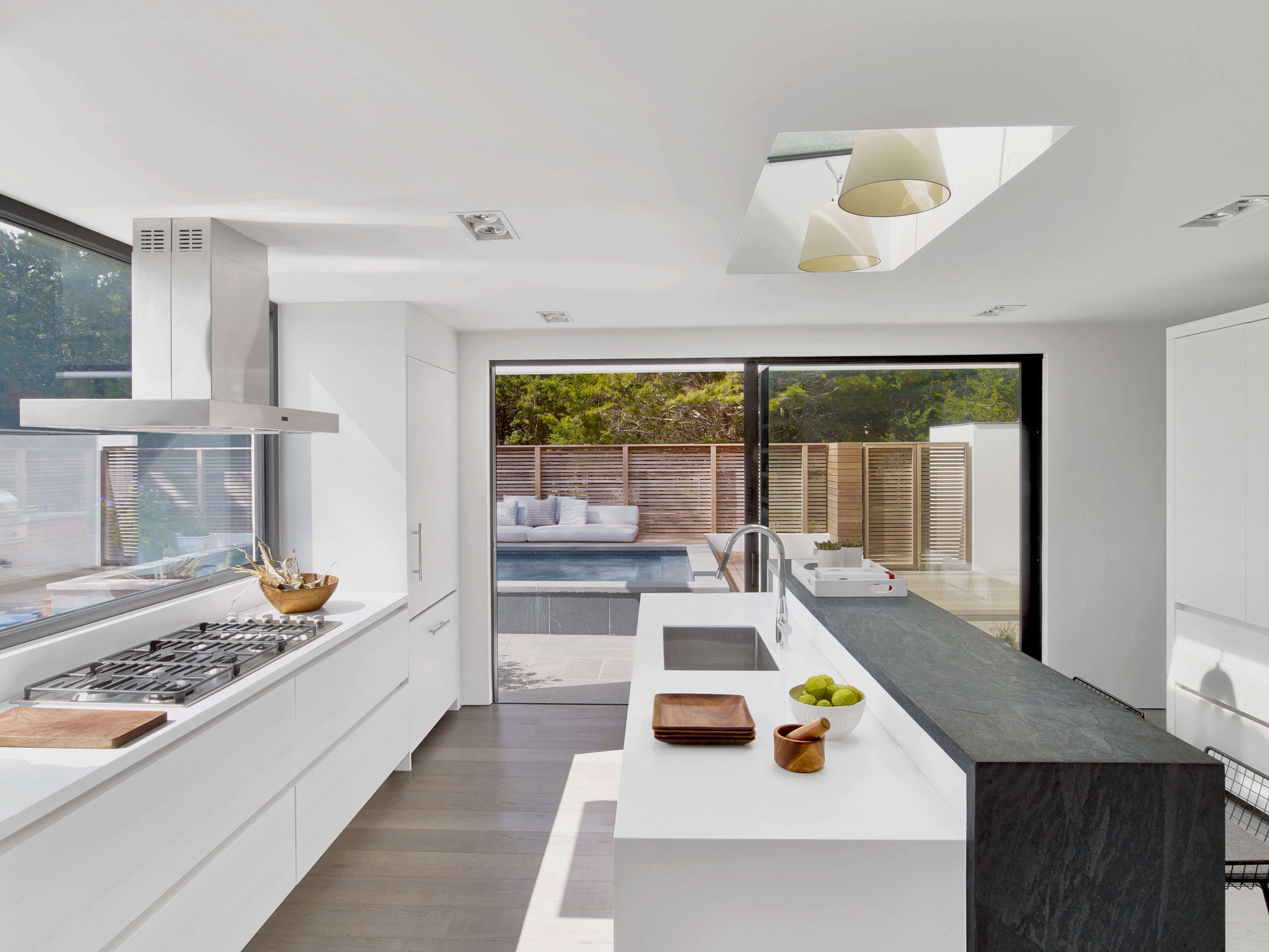 A modern kitchen with white cabinetry, a large window facing a pool area, and a sleek black countertop.