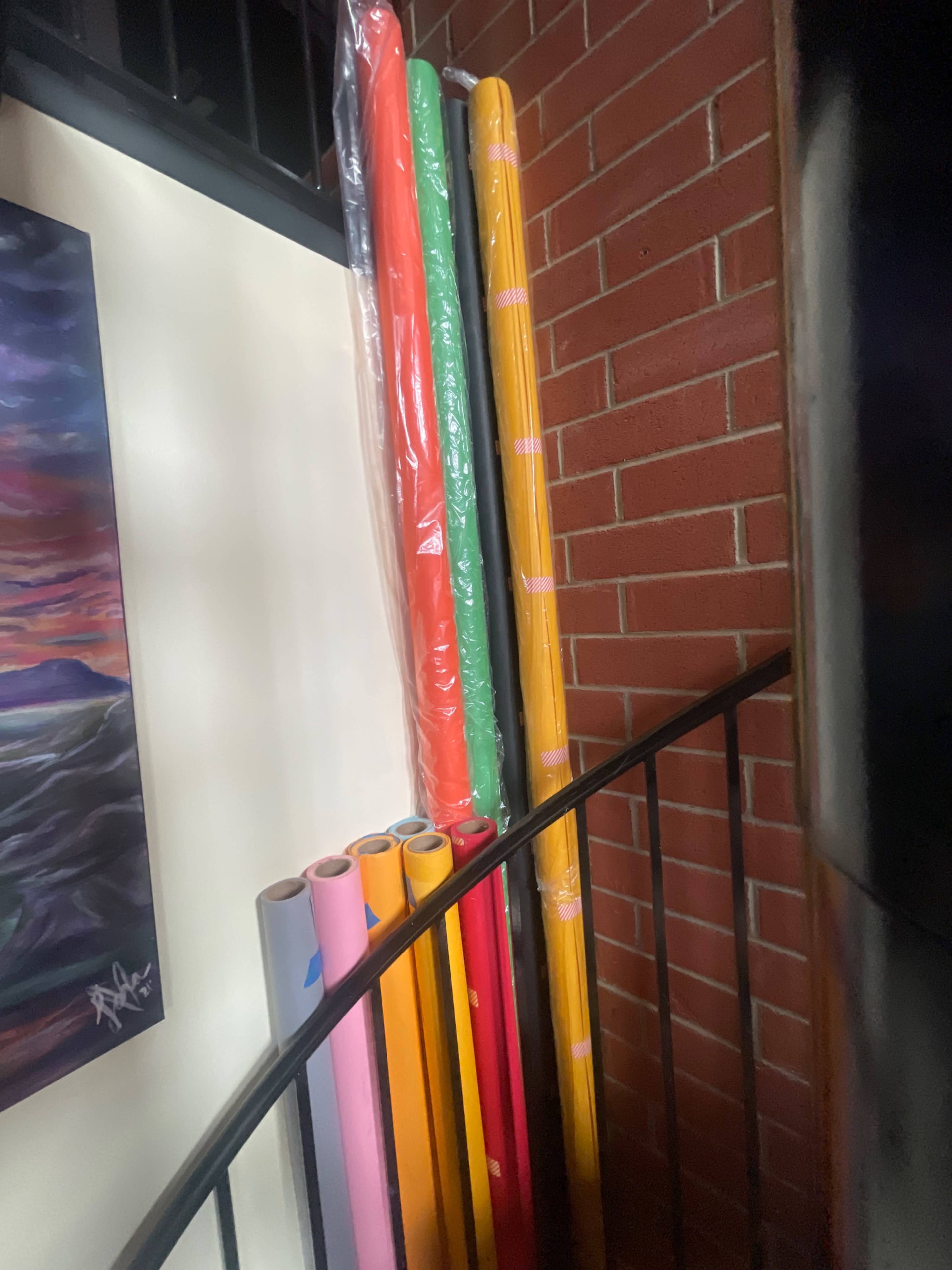 Colorful rolls of wrapping paper are stacked against a brick wall beside a staircase.