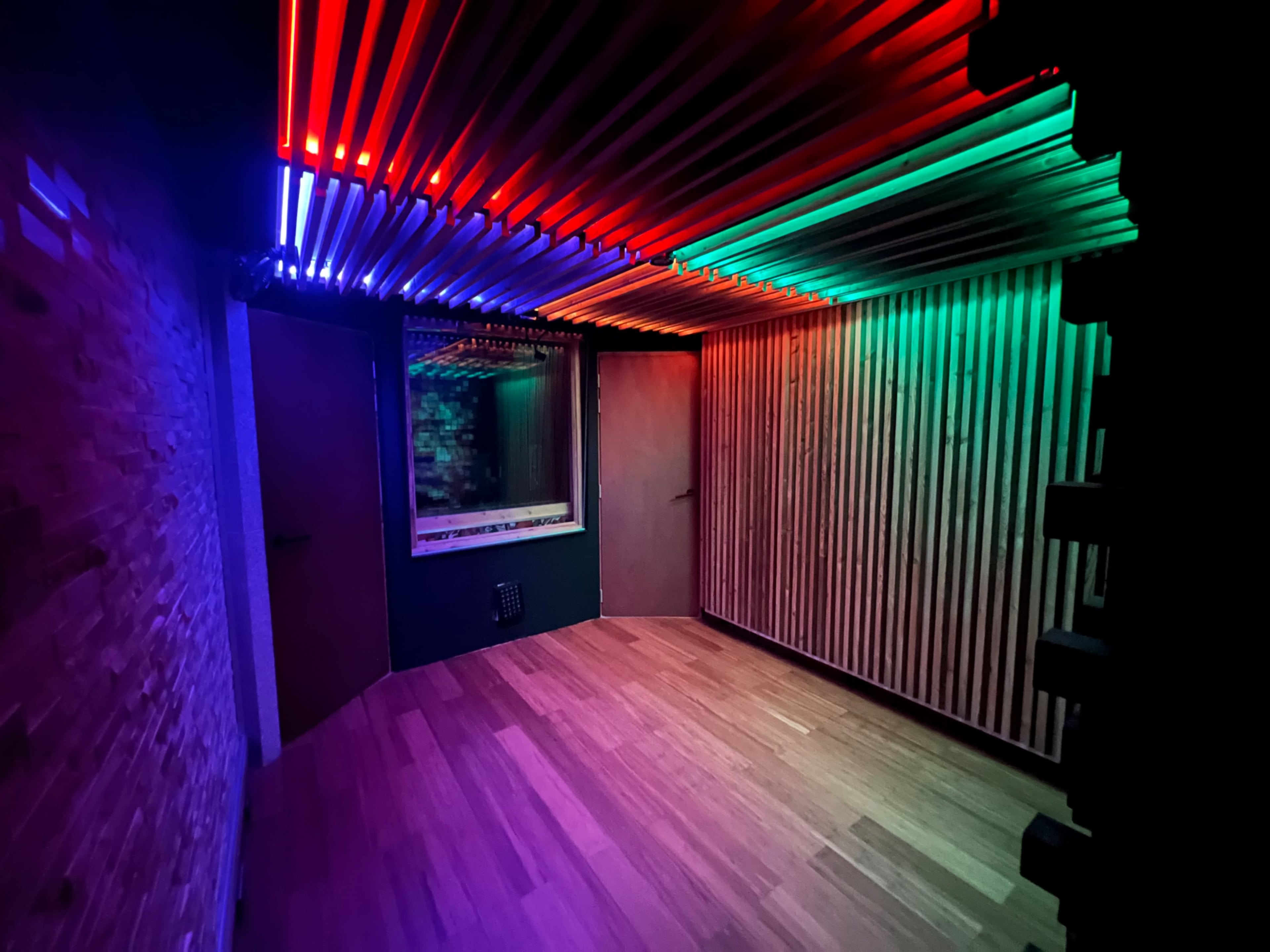 A dimly lit room with colorful LED lights mounted on the ceiling and wooden wall panels.