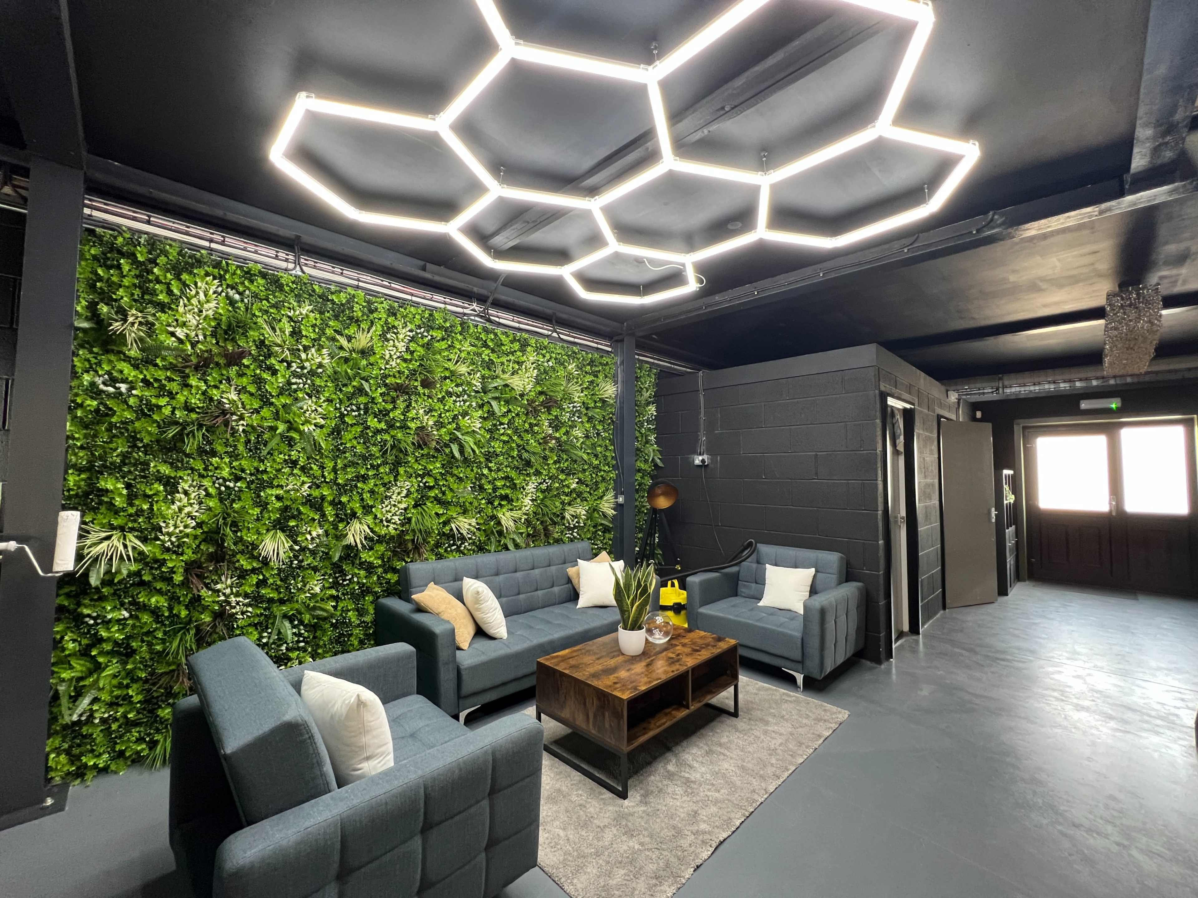 A modern lounge area features gray furniture, a wooden coffee table, and a green vertical garden wall, illuminated by a geometric light fixture.