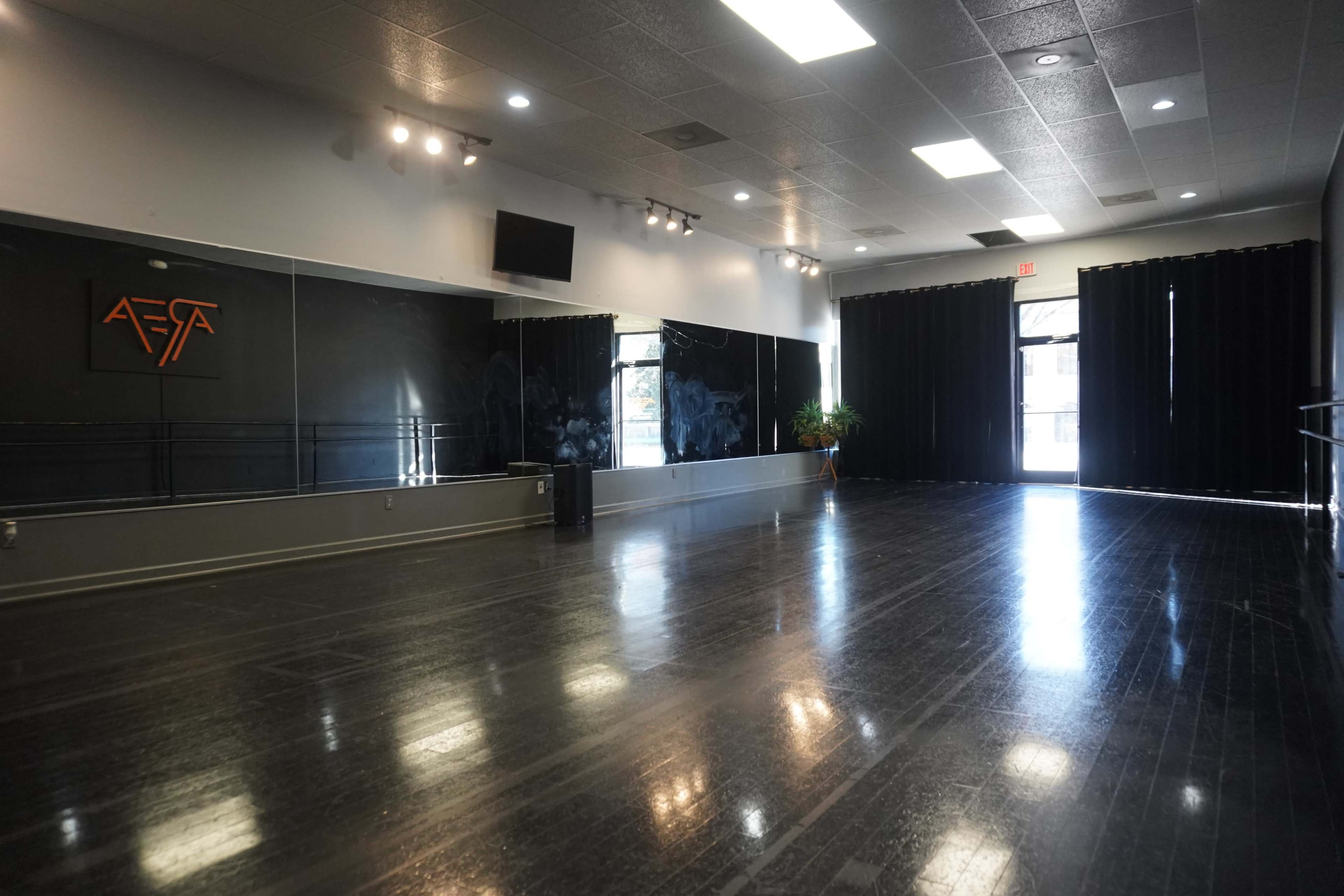 A spacious dance studio with polished wooden floors, mirrors on one wall, and large black curtains along another.