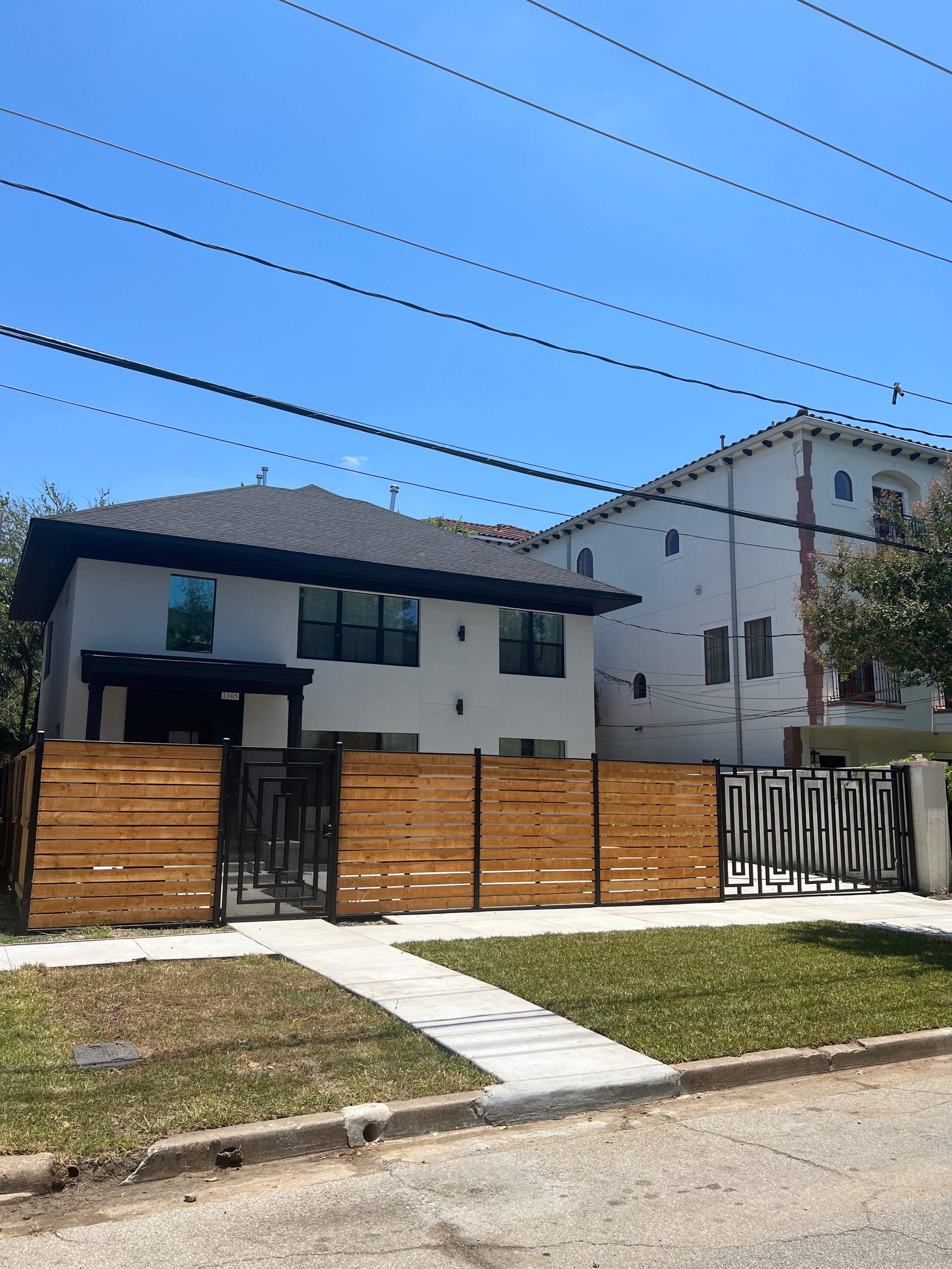 Two modern houses stand across from each other, with one featuring a wooden fence and a sidewalk in front.