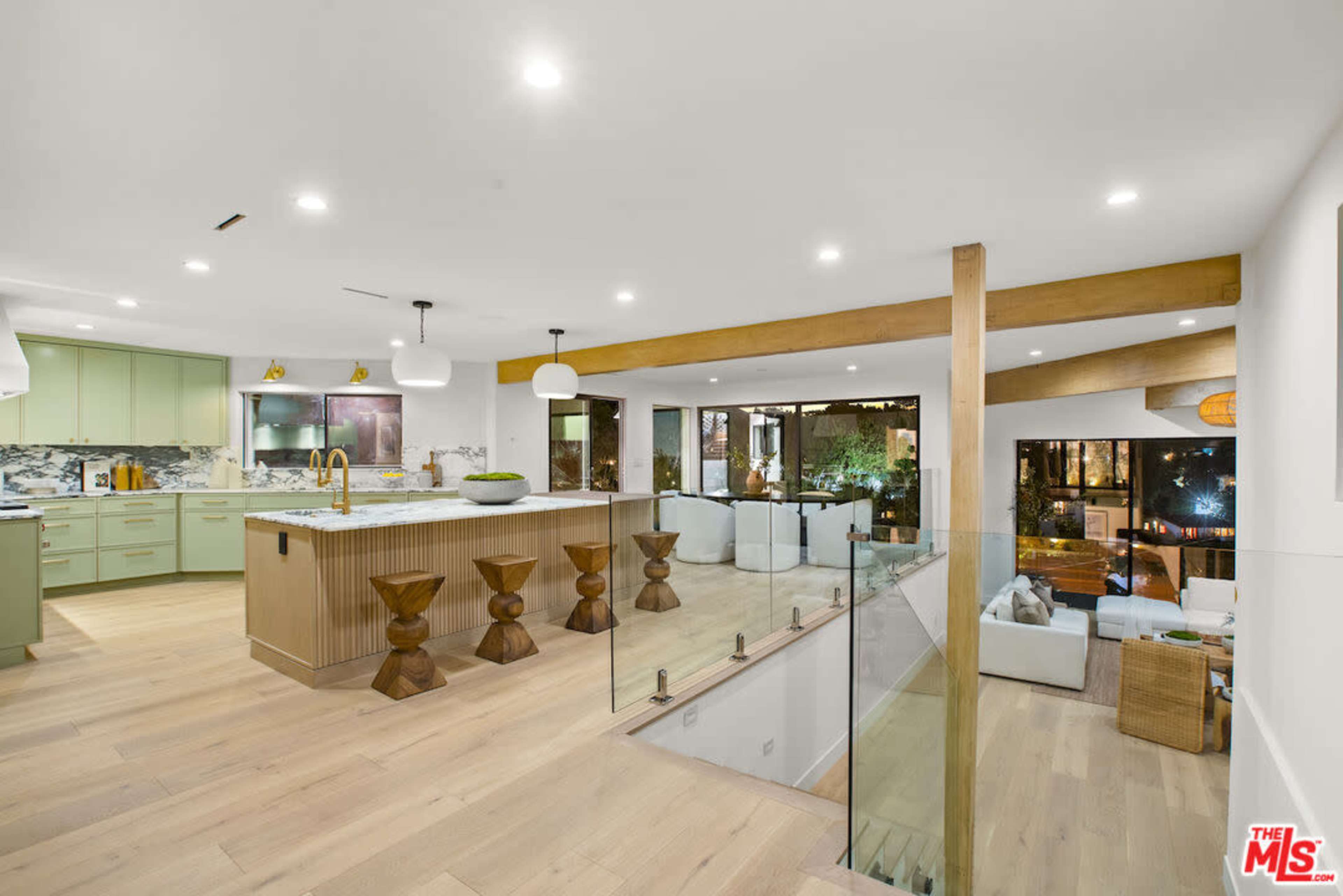 A modern open-concept kitchen and living area features wooden elements, sleek cabinetry, and large windows overlooking a garden.