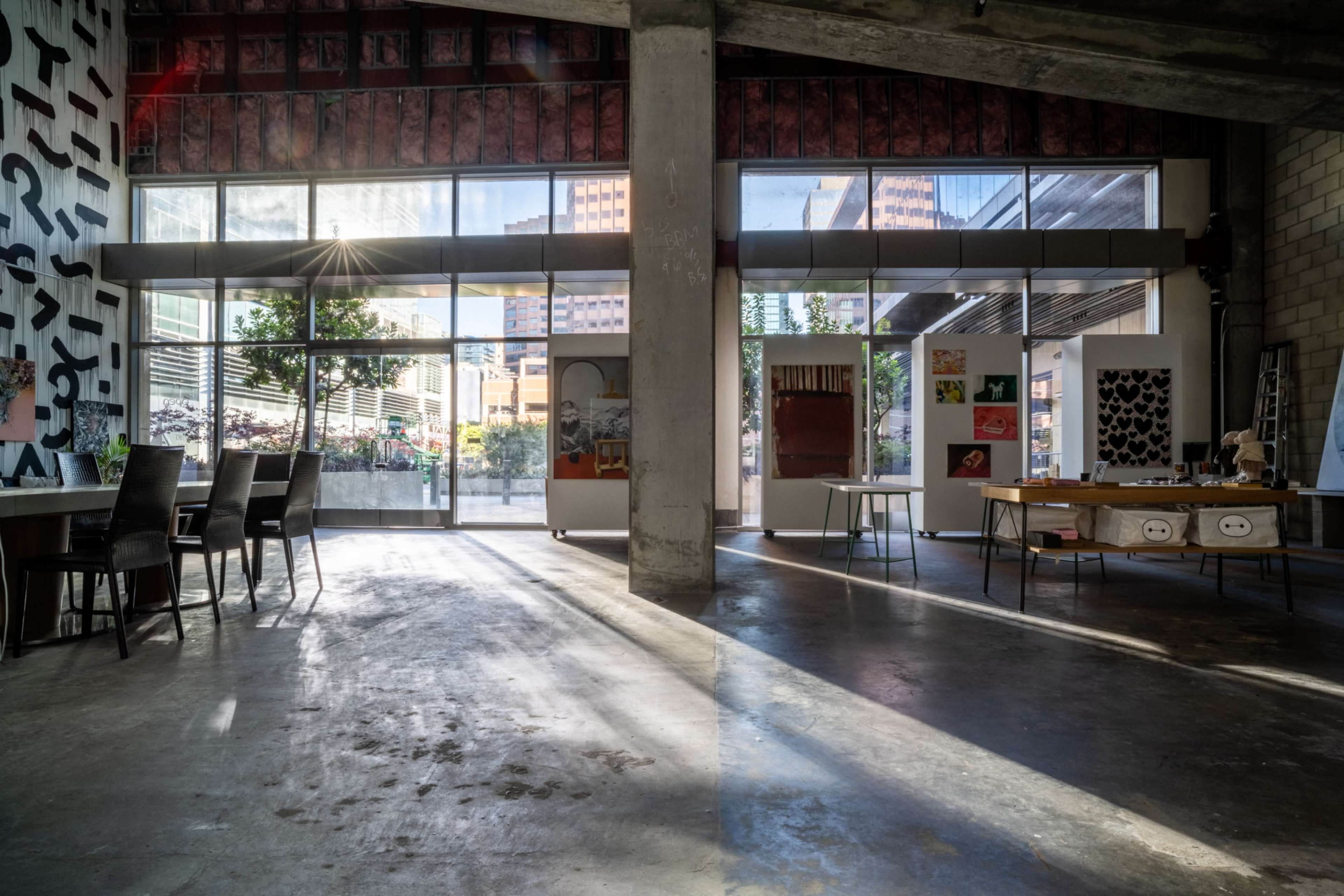 The image shows a spacious contemporary interior with large windows, allowing natural light to stream in, illuminating furniture and art displays.