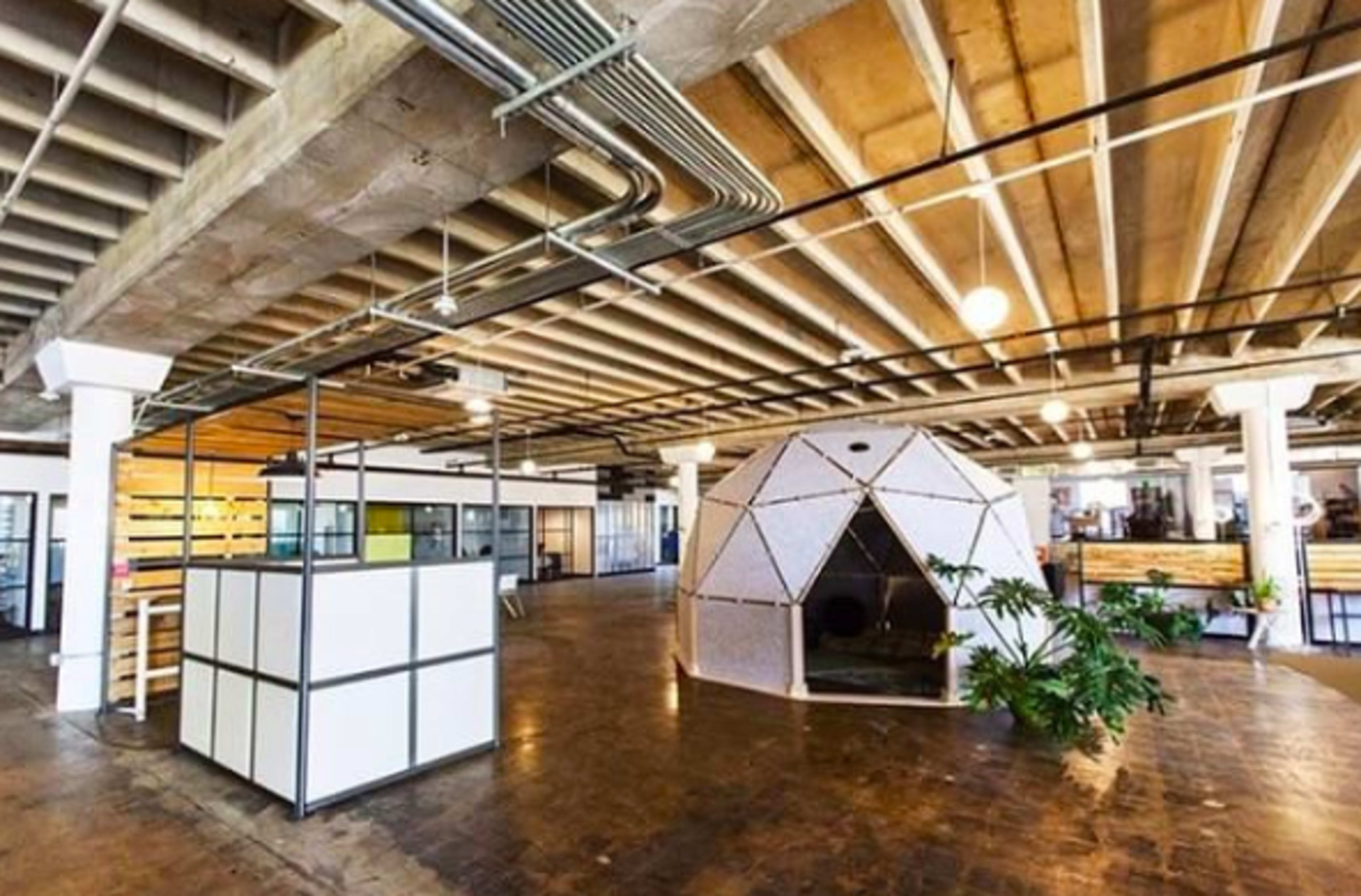 The image shows a modern open office space featuring a geodesic dome structure in the center, surrounded by partitioned areas and industrial-style design elements.