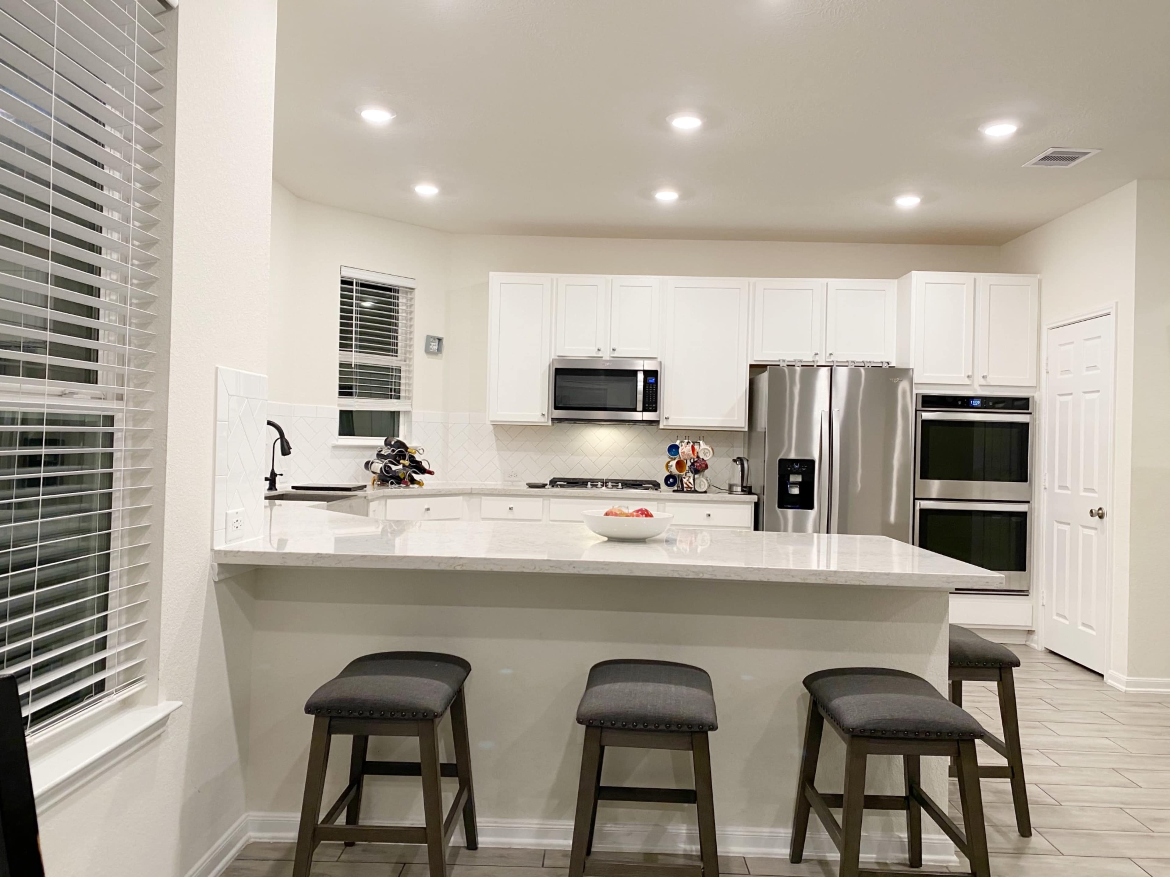 A modern kitchen with white cabinetry, stainless steel appliances, and a central island with four stools.