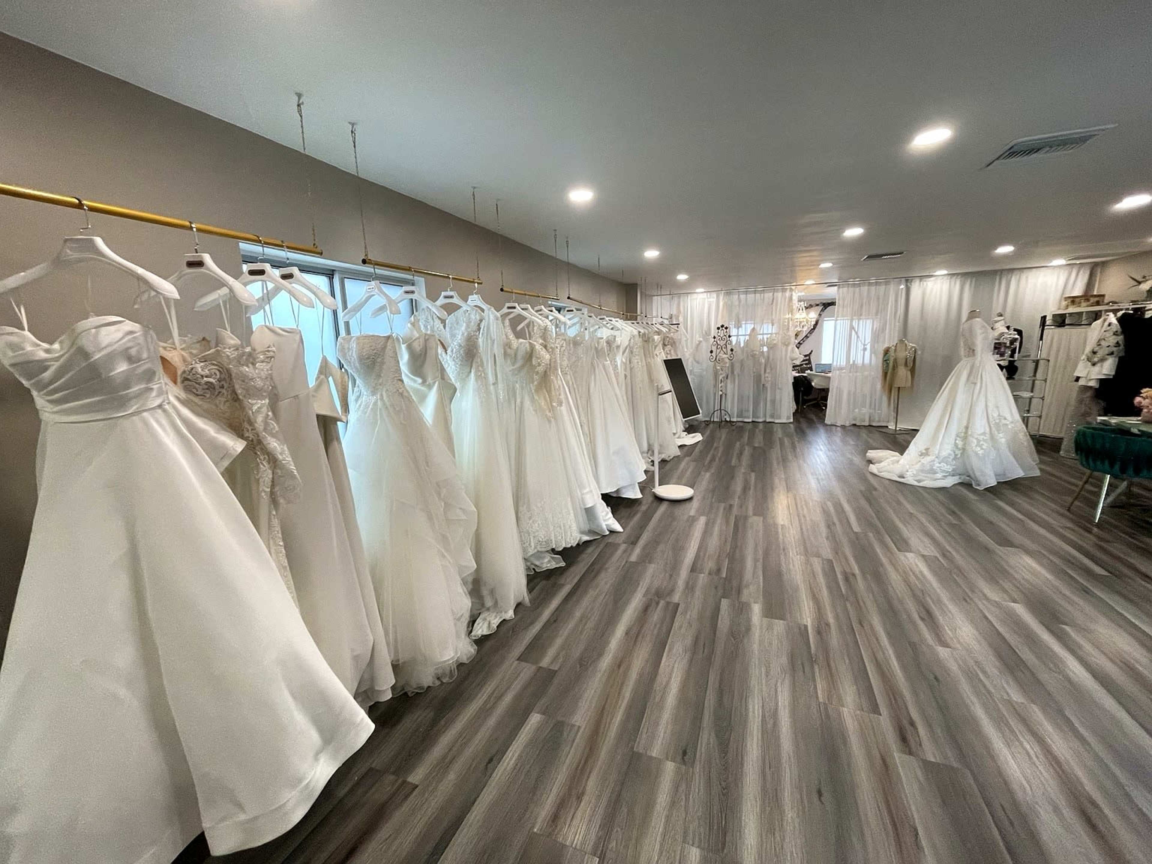 The image shows a bridal shop interior with several wedding dresses displayed on hangers along one wall.